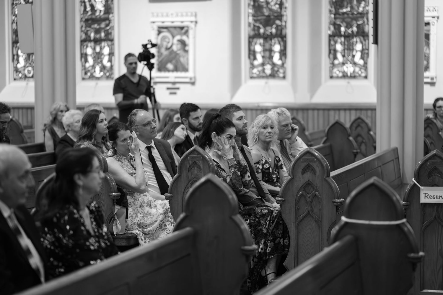 Wedding congregation gathered in wooden pews beneath stained glass windows.