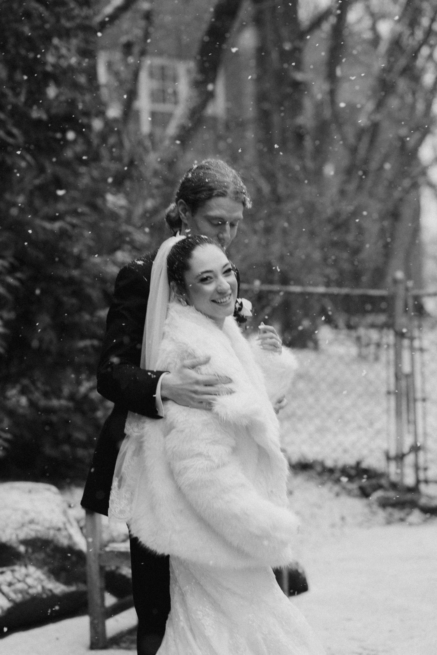 A romantic black and white winter wedding portrait with snow falling in the background.