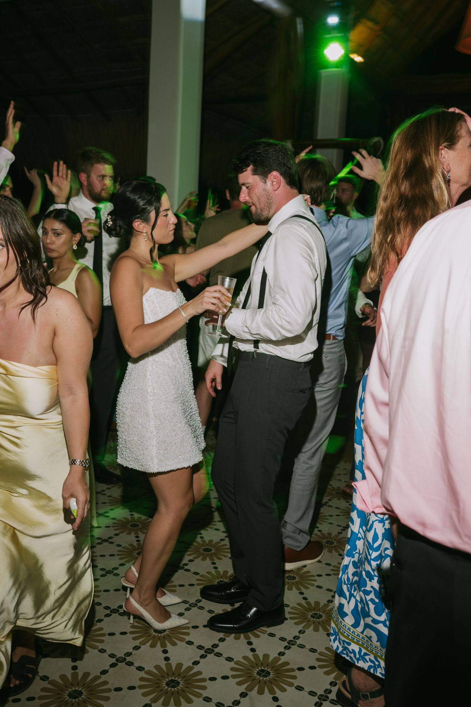 Reception guests dance and celebrate on a decorated dance floor with green lighting effects.