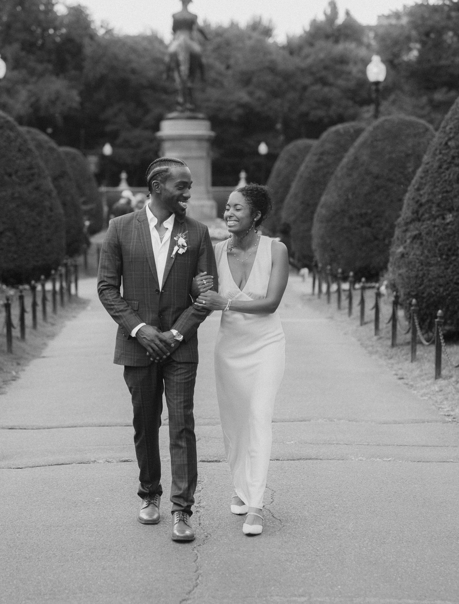Joyful couple walking and laughing together along garden path lined with topiaries.