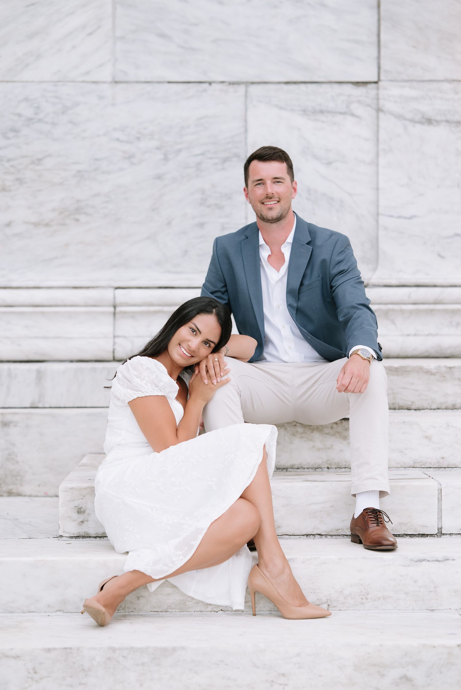 Couple in white clothing posing on marble steps during engagement session.