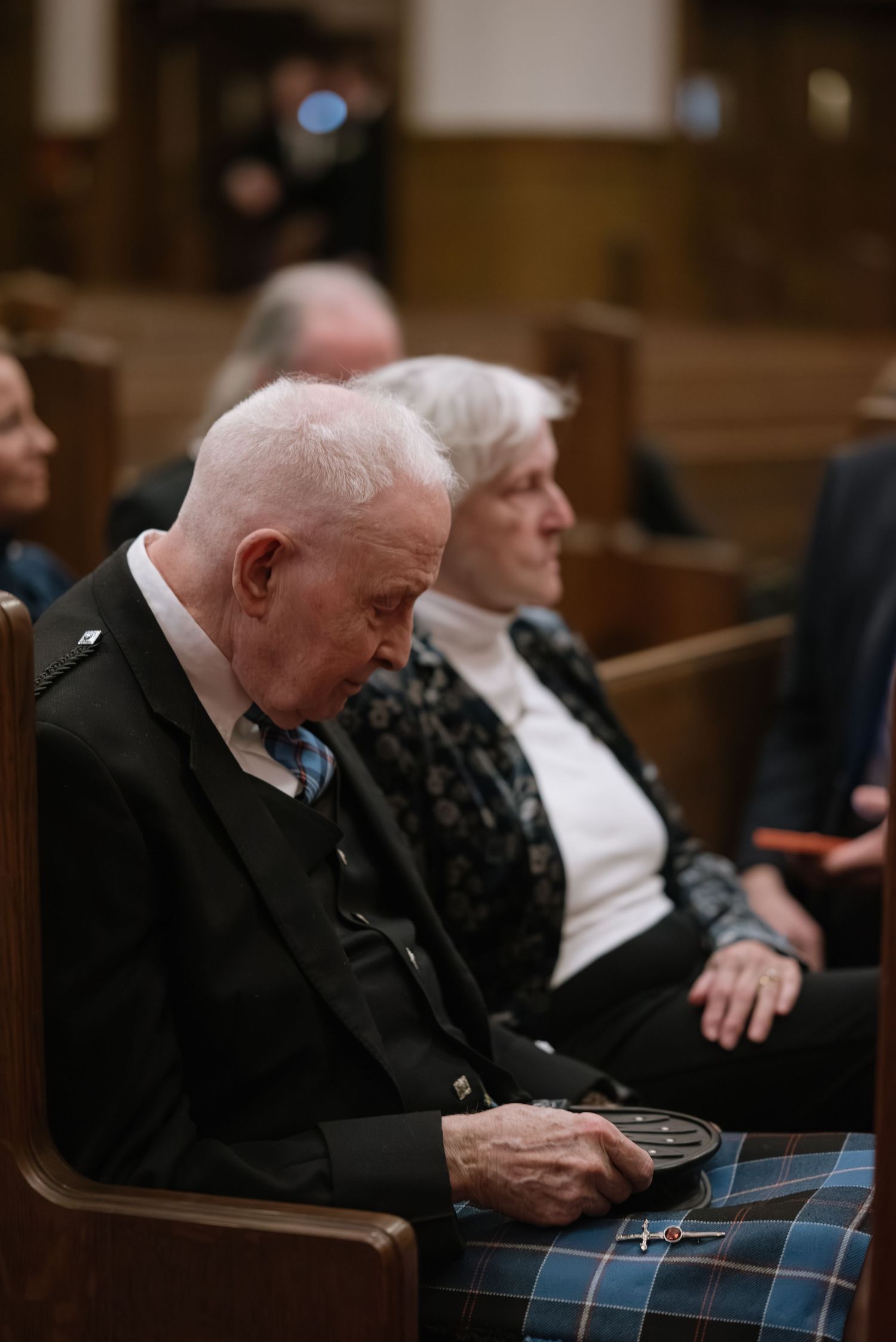 Guests in formal attire seated in wooden pews during a church ceremony.