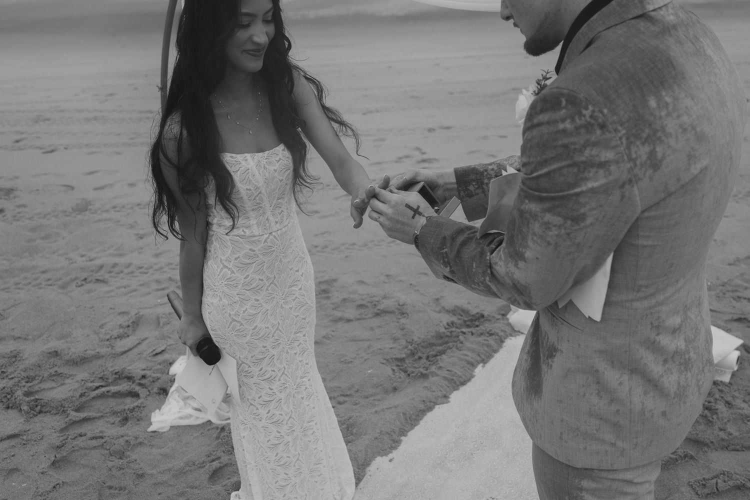 Couple in formal attire sharing romantic moments during a black and white beach photoshoot.