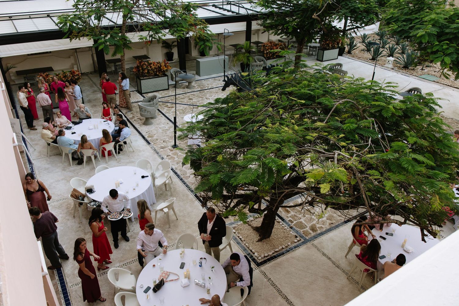 Indoor atrium event space with high glass ceiling, tropical plants and gathered attendees.