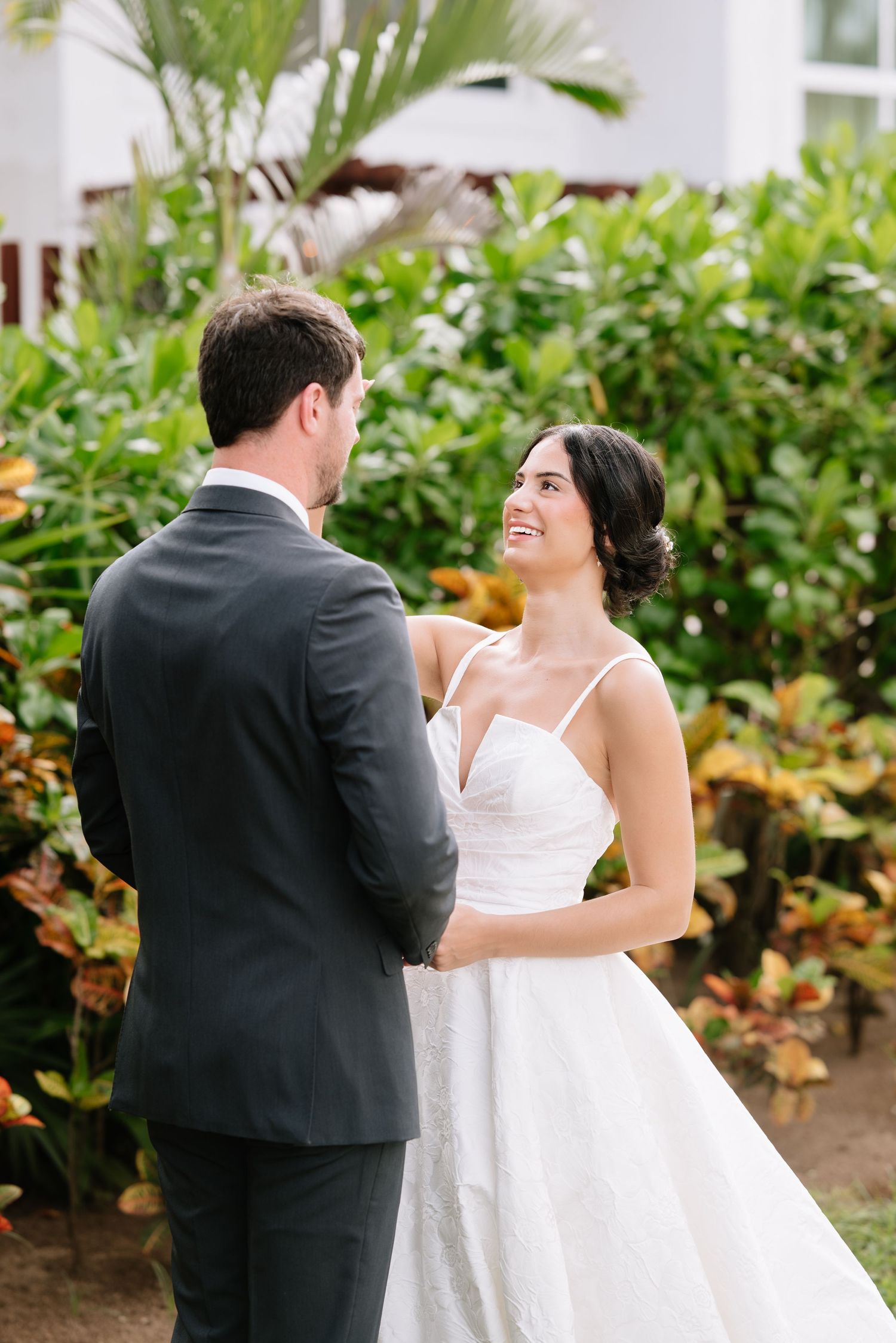 A couple shares a joyful moment during their first look in a lush garden setting.