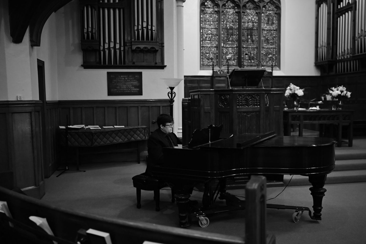 Interior view of a church sanctuary showing ornate stained glass windows and multiple pianos arranged in a row.