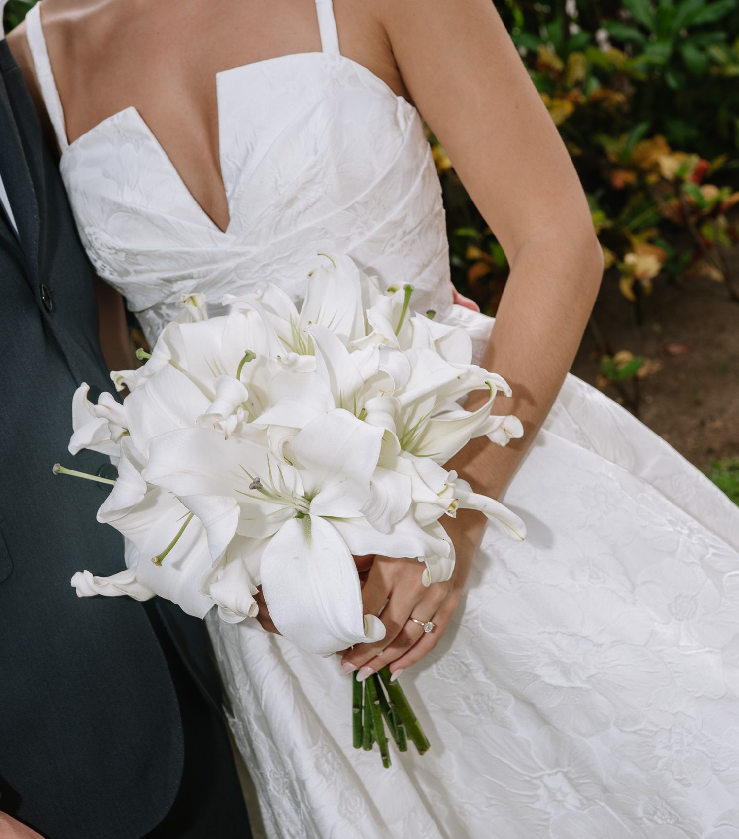 Close-up details of elegant white lily wedding bouquet and bridal gown.
