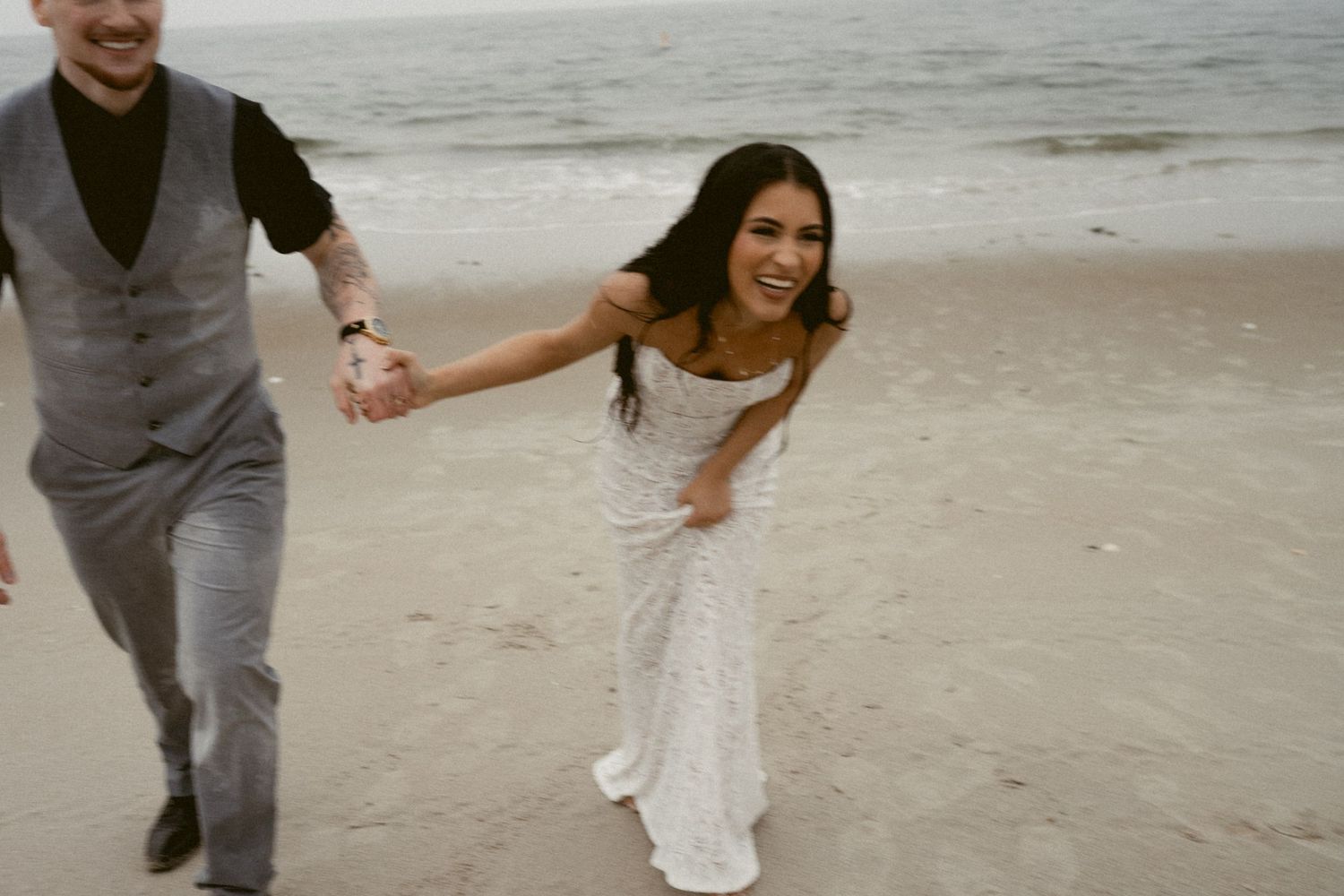 A joyful couple runs playfully along the beach during their wedding celebration.