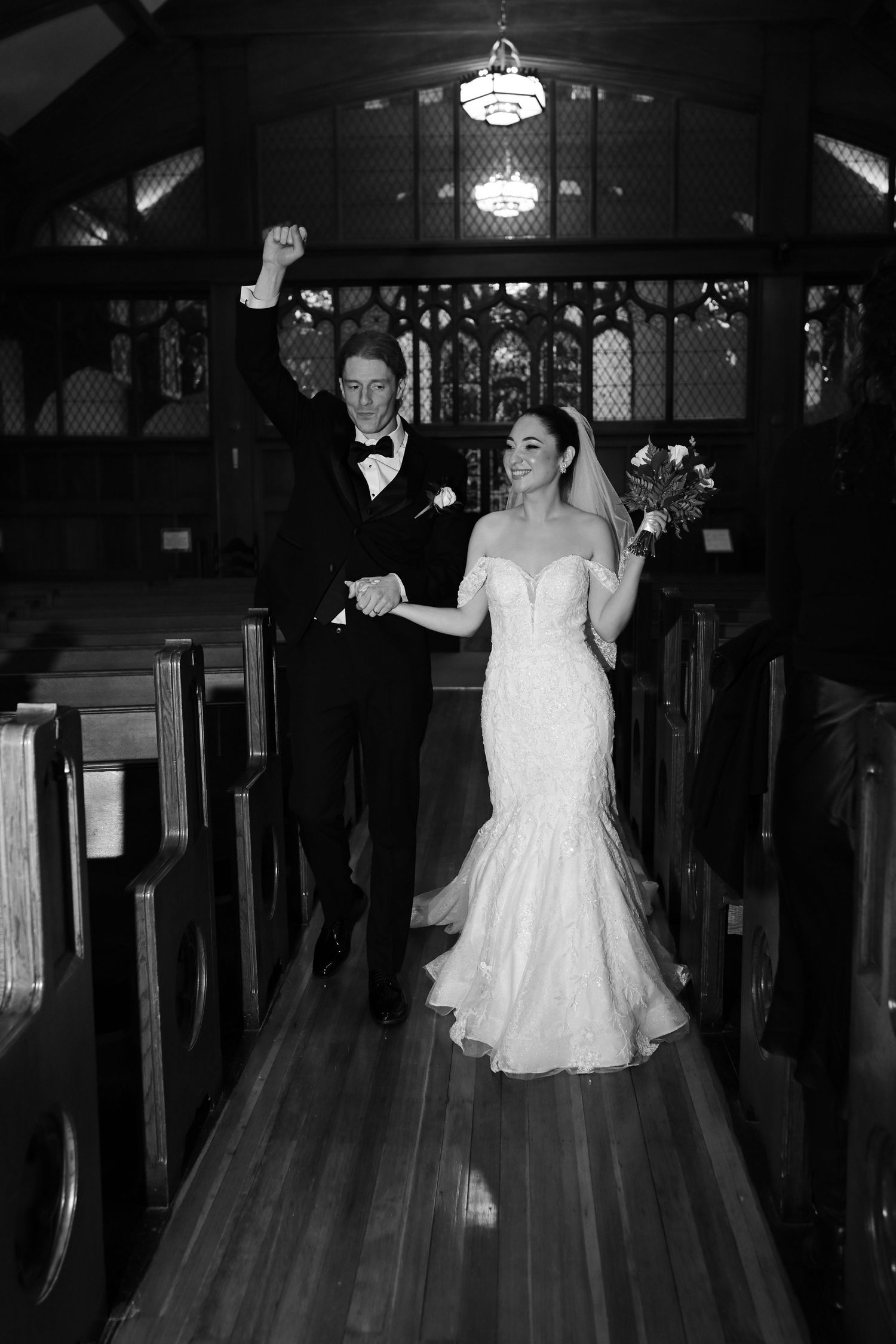 A newlywed couple walks down the church aisle after their ceremony in black and white.