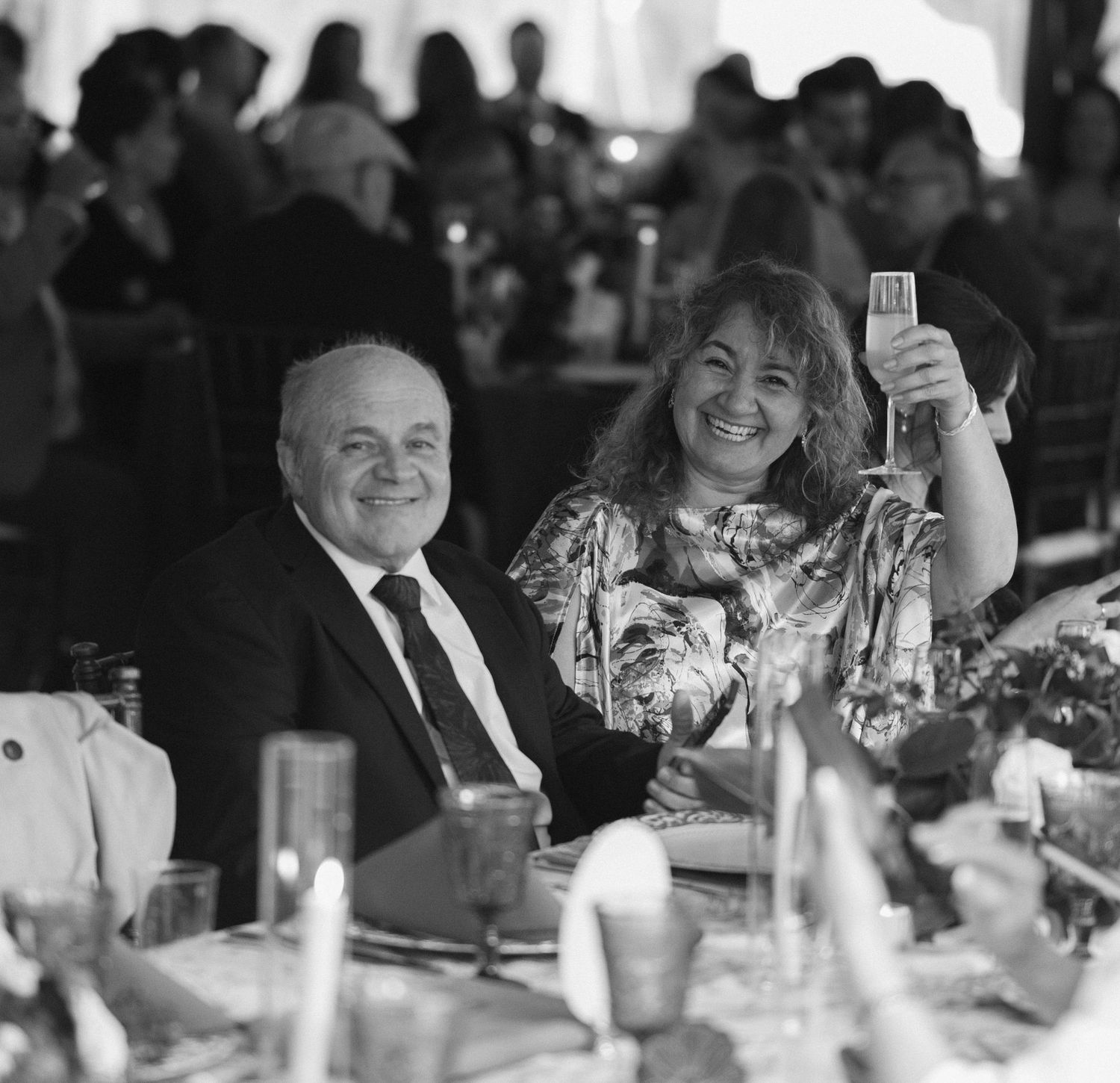 A smiling couple toasting at a wedding reception dinner in a black and white photo.