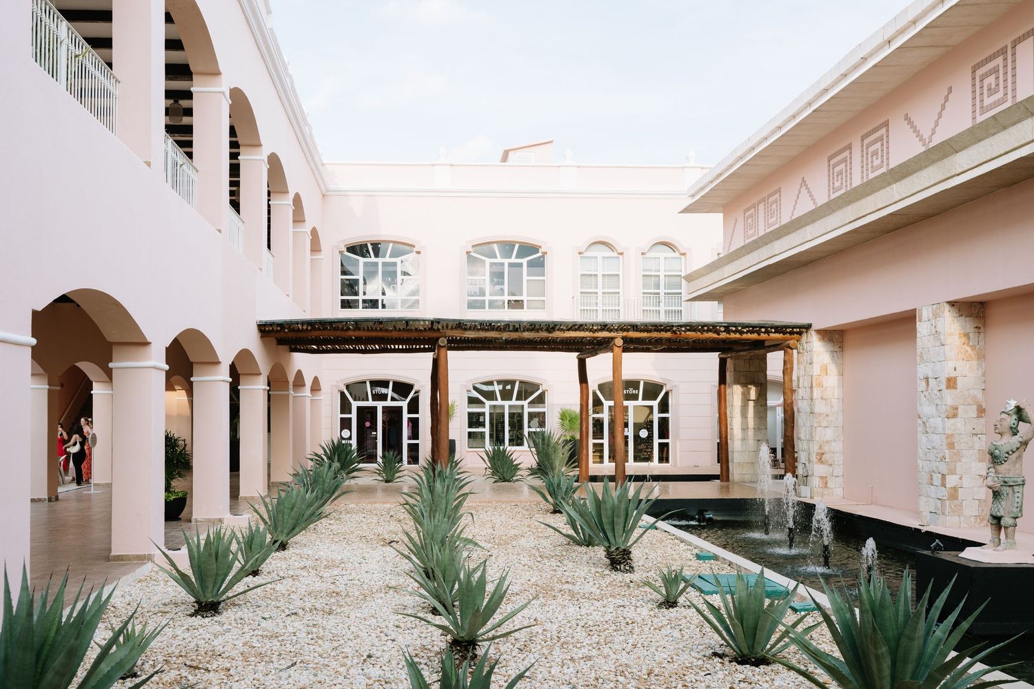 Modern courtyard with beige stucco buildings, archways and desert landscaping featuring agave plants.