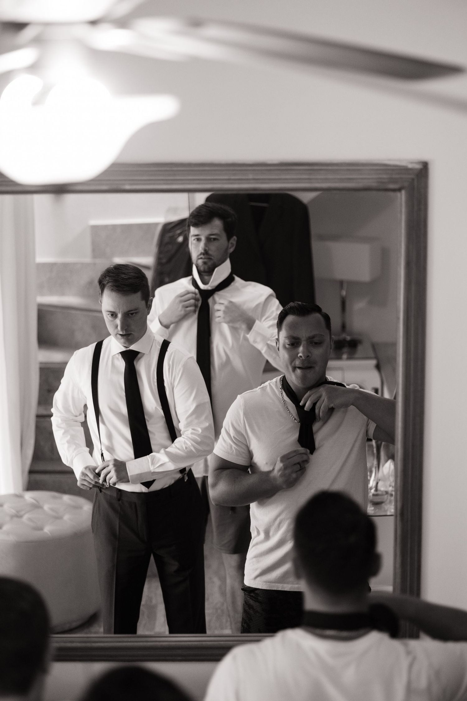 Black and white photo sequence showing men in white shirts and suspenders getting ready in front of a mirror.