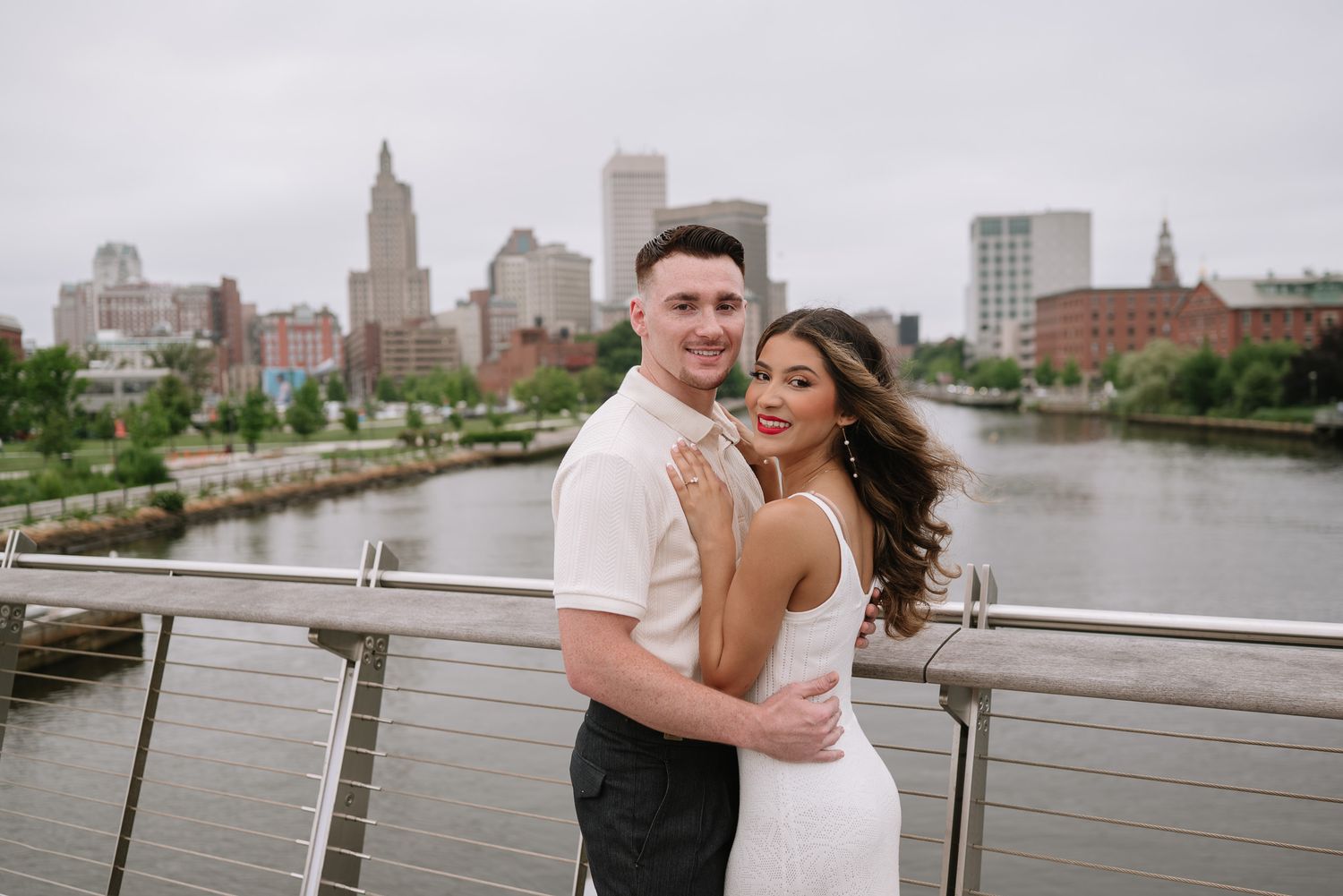 Romantic couple posing on waterfront with city skyline in background.