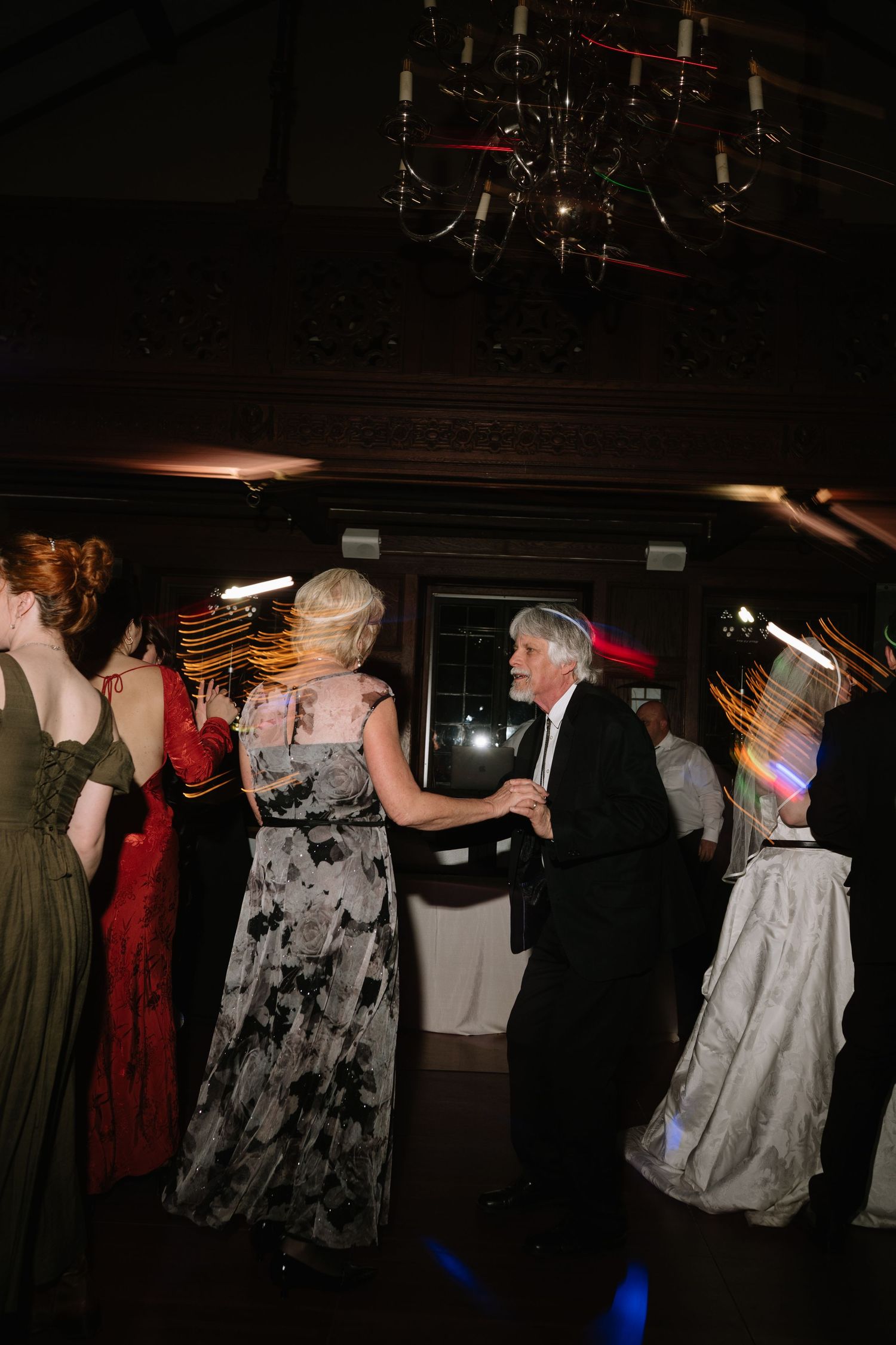 Guests dance energetically under a chandelier at a formal wedding reception with colorful light effects.