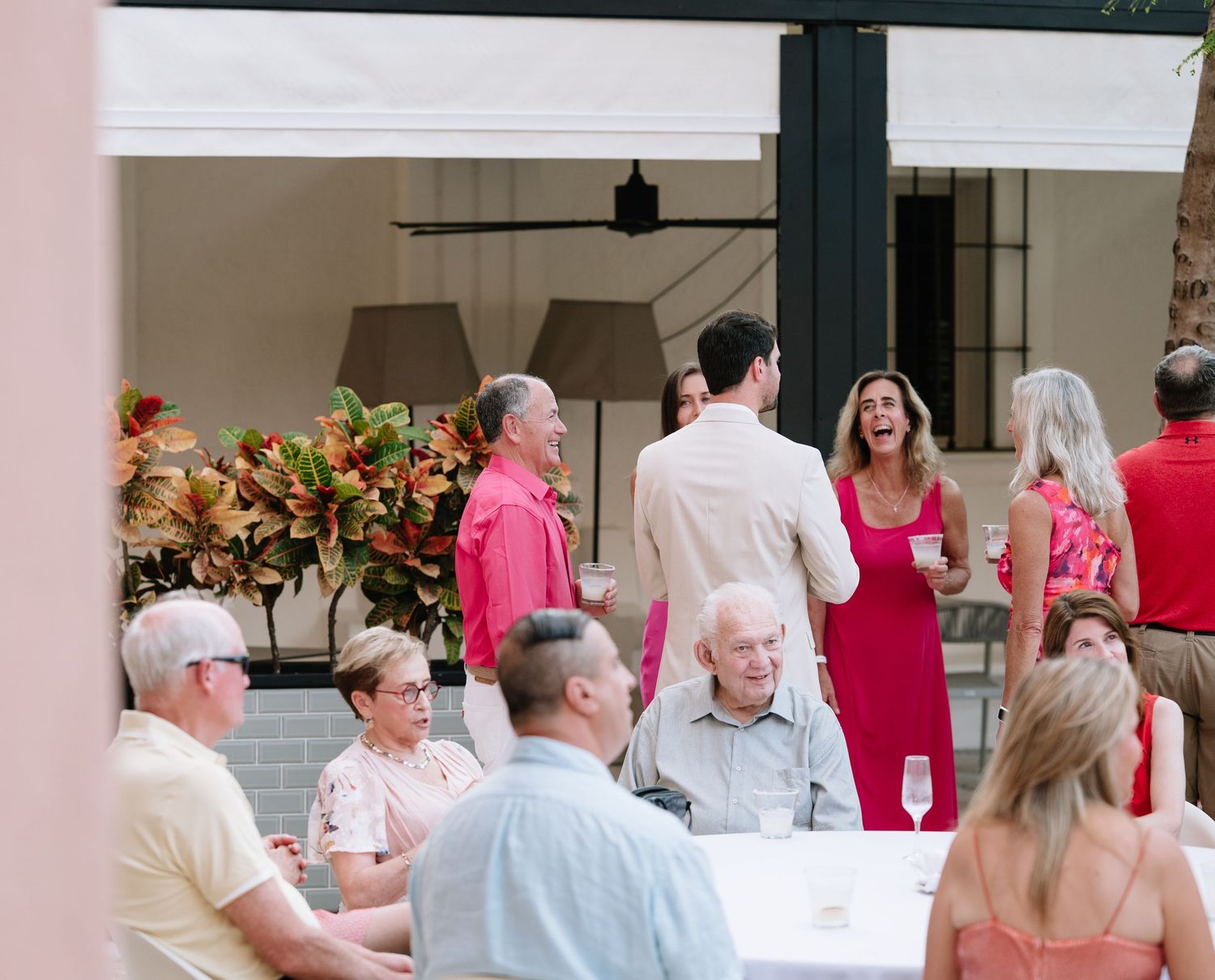 Wedding guests seated at round tables in a reception hall with pink and white decor.