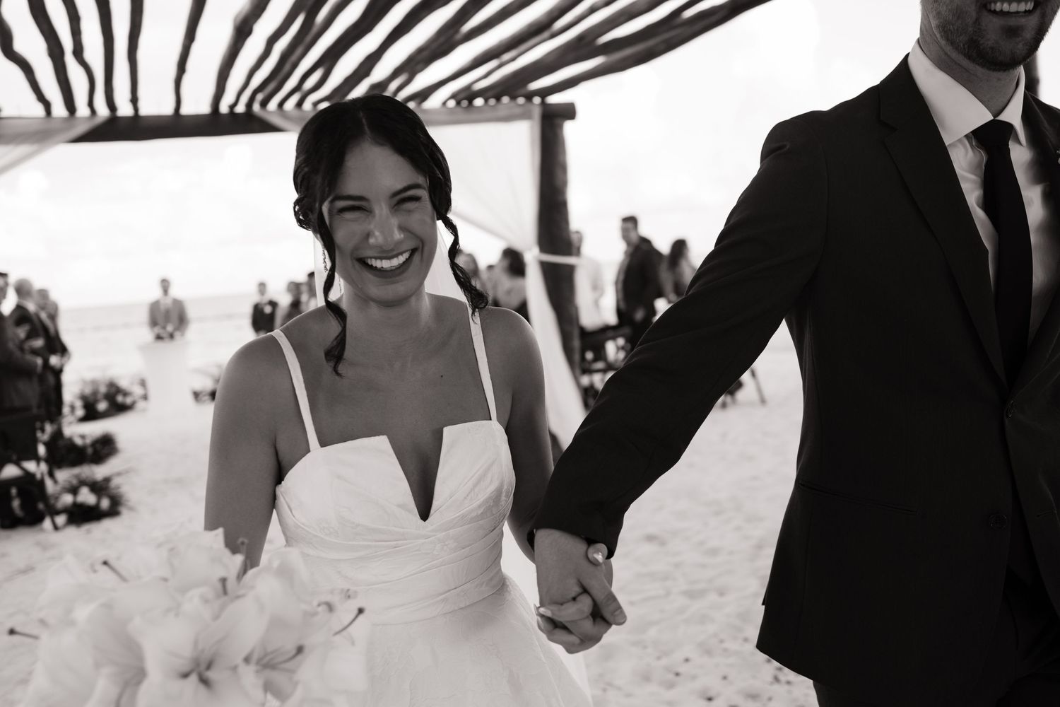 Wedding party members walking and celebrating on a beach with palm trees in the background.