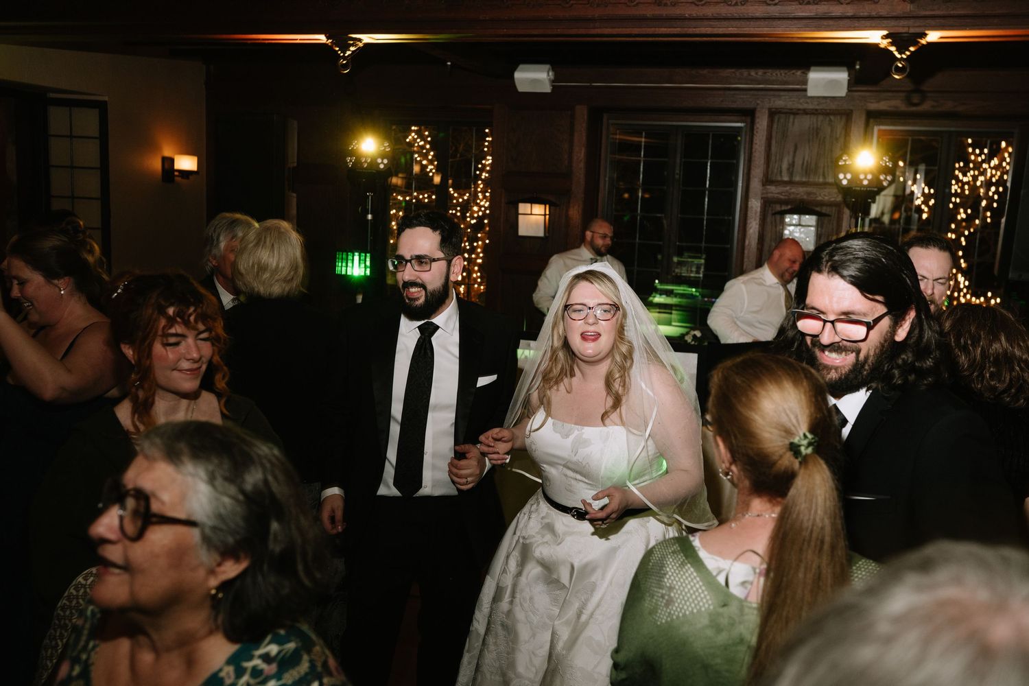 Bride and groom share a joyful moment on the dance floor surrounded by wedding guests at an elegant indoor reception.