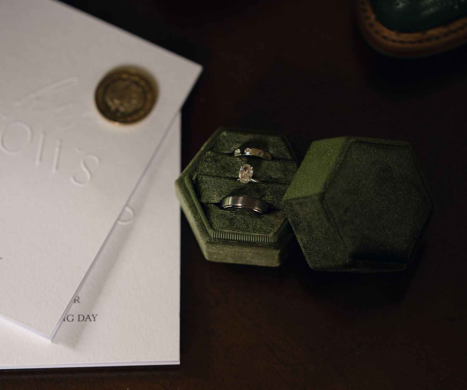 Green velvet hexagonal ring box with wedding bands and diamond ring beside an elegant wedding day card.