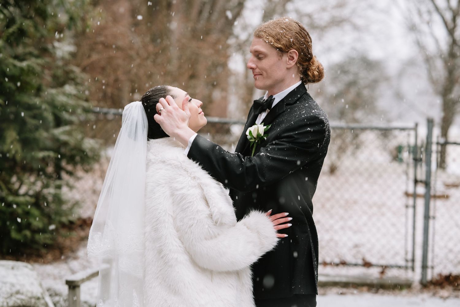 A winter wedding portrait showing a couple embracing in falling snow.