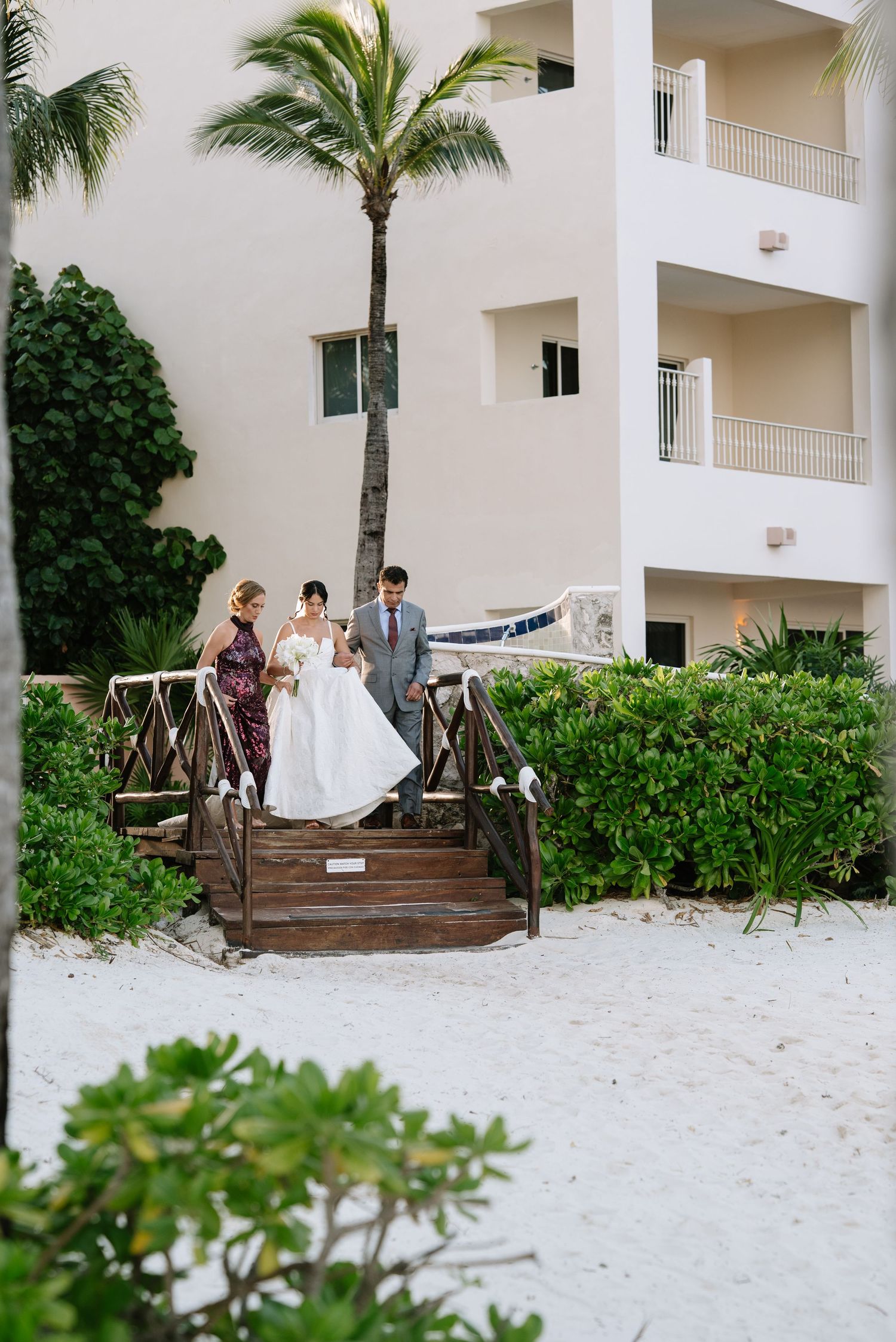 Wedding ceremony setup on a tropical beach with palm trees and white hotel building in the background.