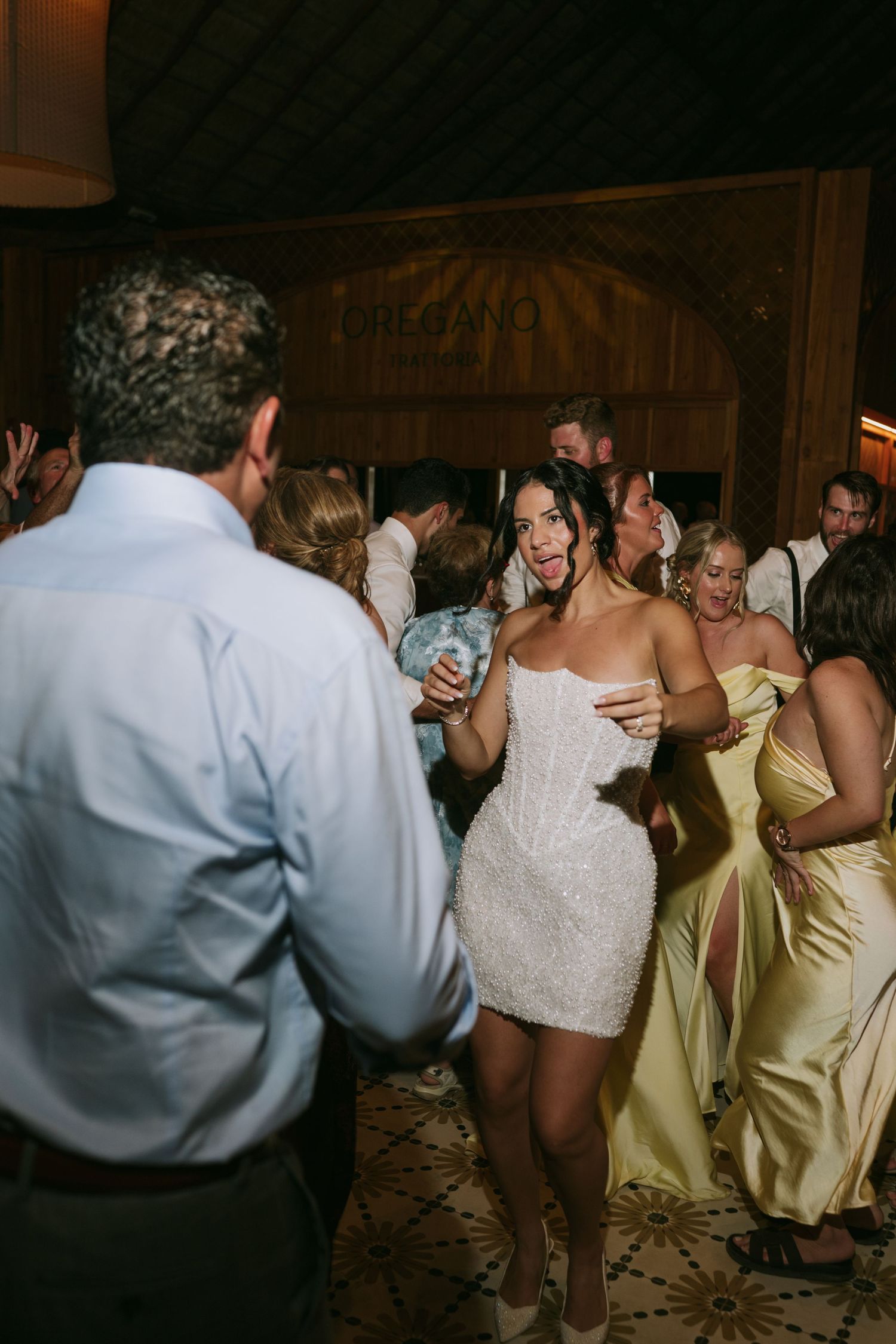 Wedding guests dance energetically in formal attire under dim lighting at reception.