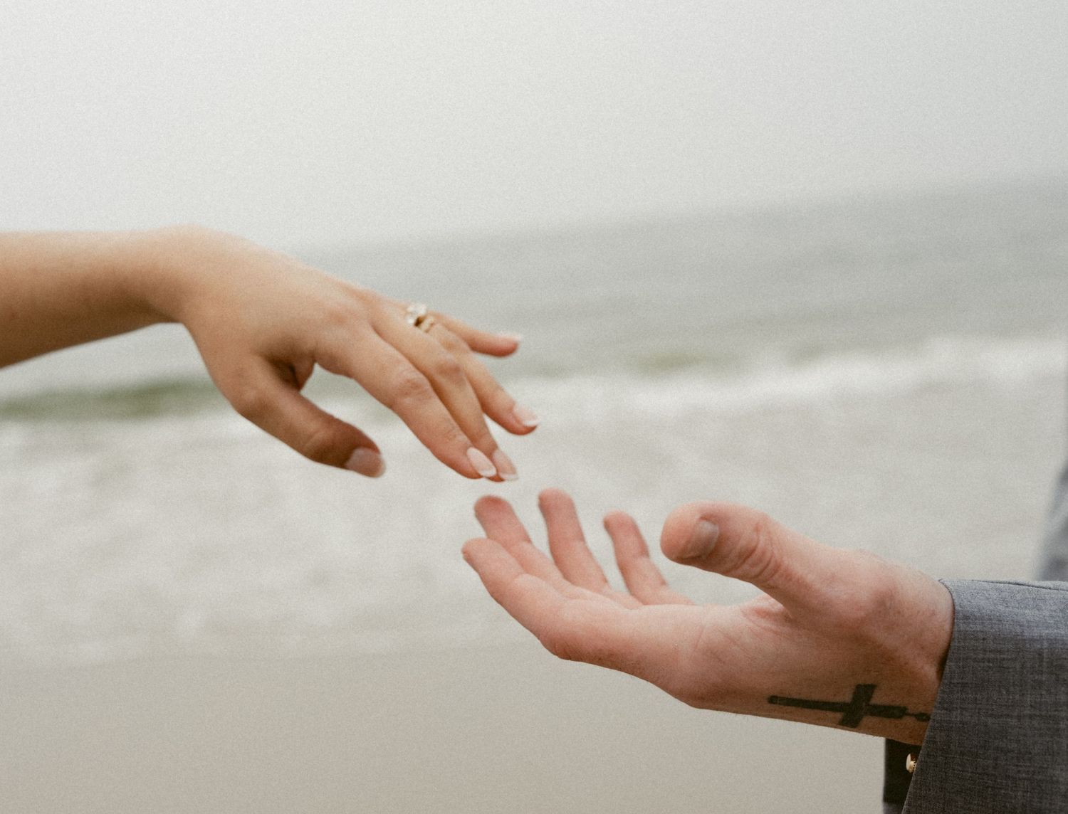 Close-up of hands exchanging a wedding ring on a cloudy beach.