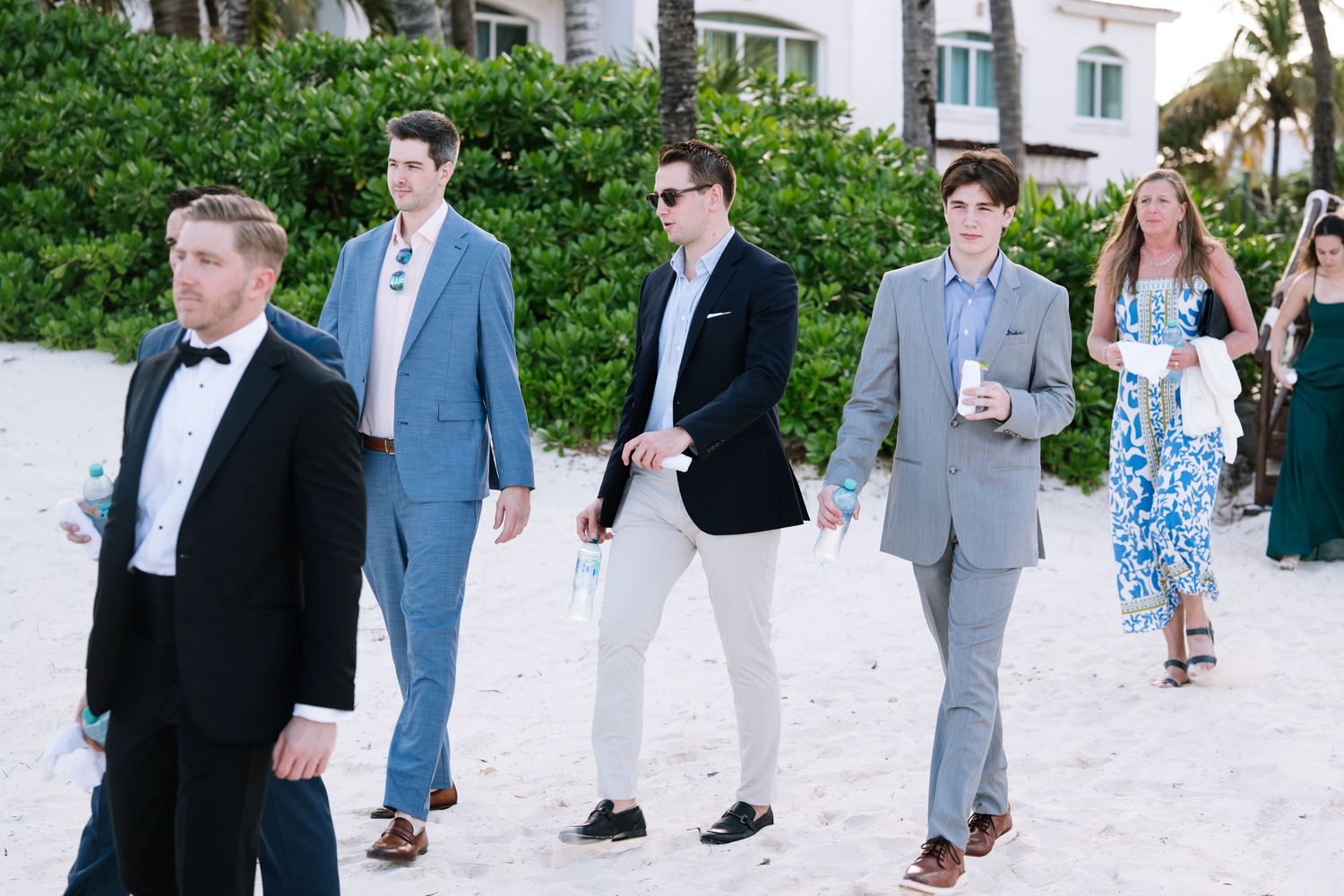 A group of formally dressed guests mingling at an outdoor wedding reception on a white gravel path.