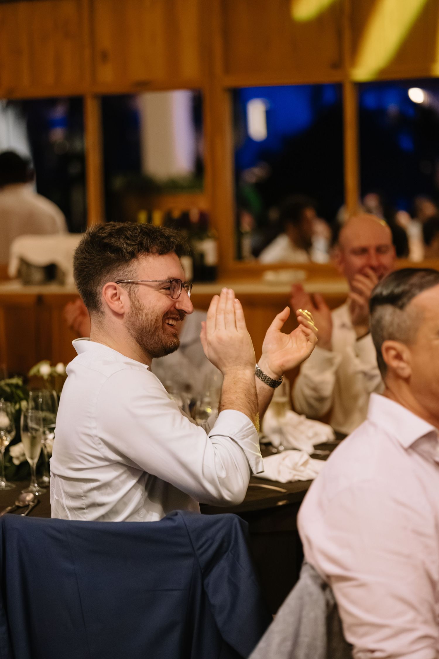 Wedding guests share laughter and emotional moments during a reception dinner at a rustic venue.