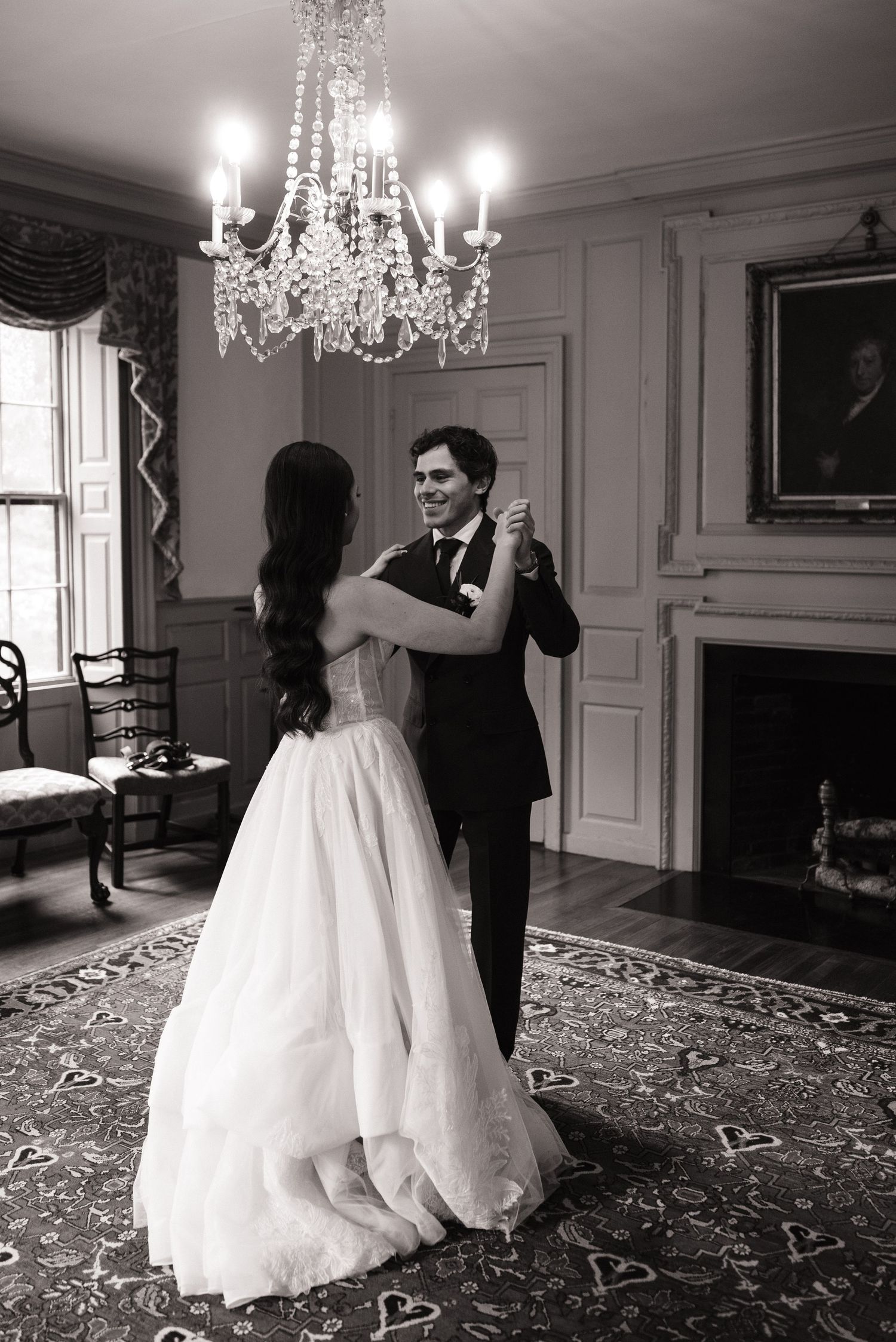 Bride and groom share their first dance in an elegant chandelier-lit ballroom in black and white photo.