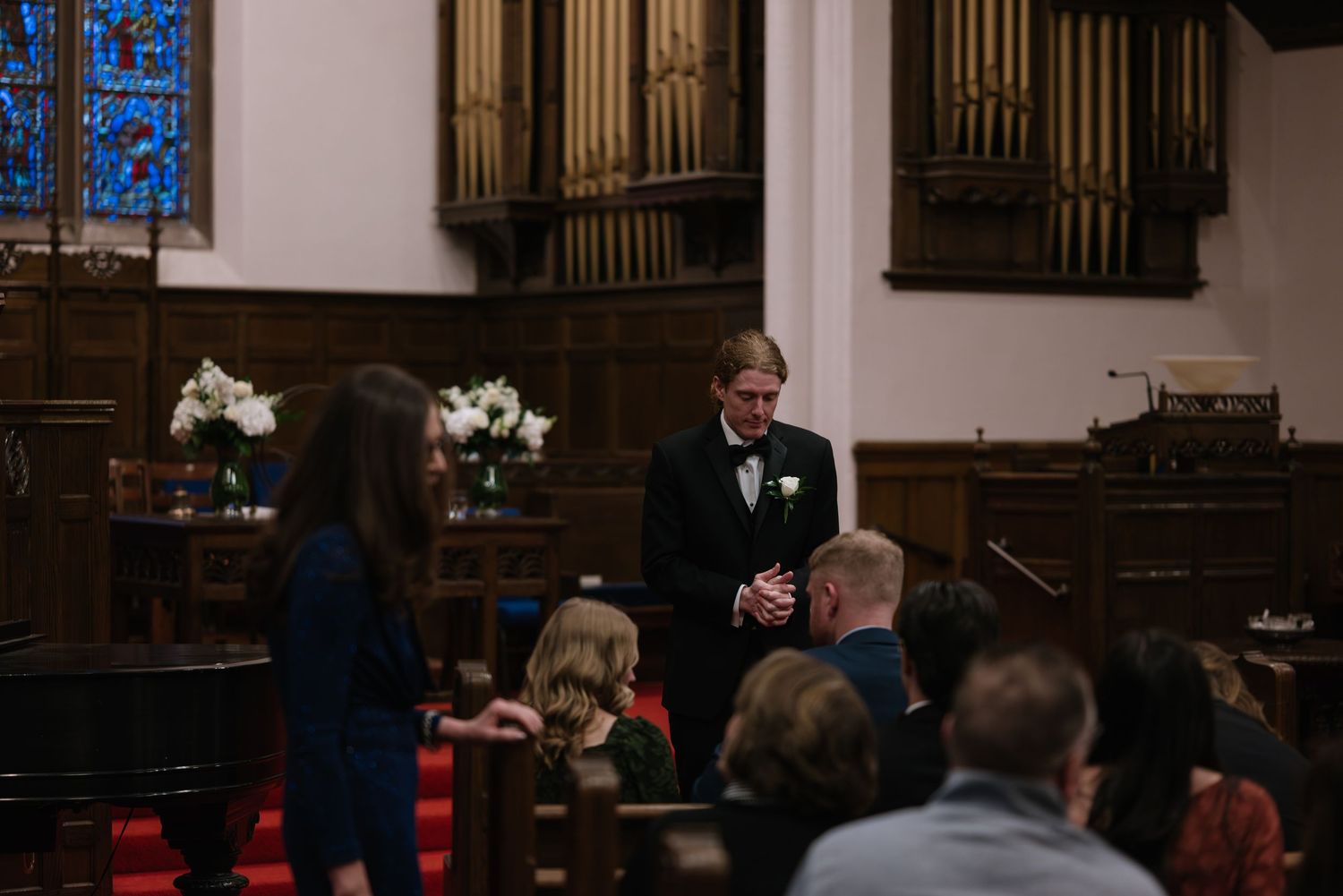 Interior of church sanctuary with wooden pews and organ pipes visible during wedding ceremony.