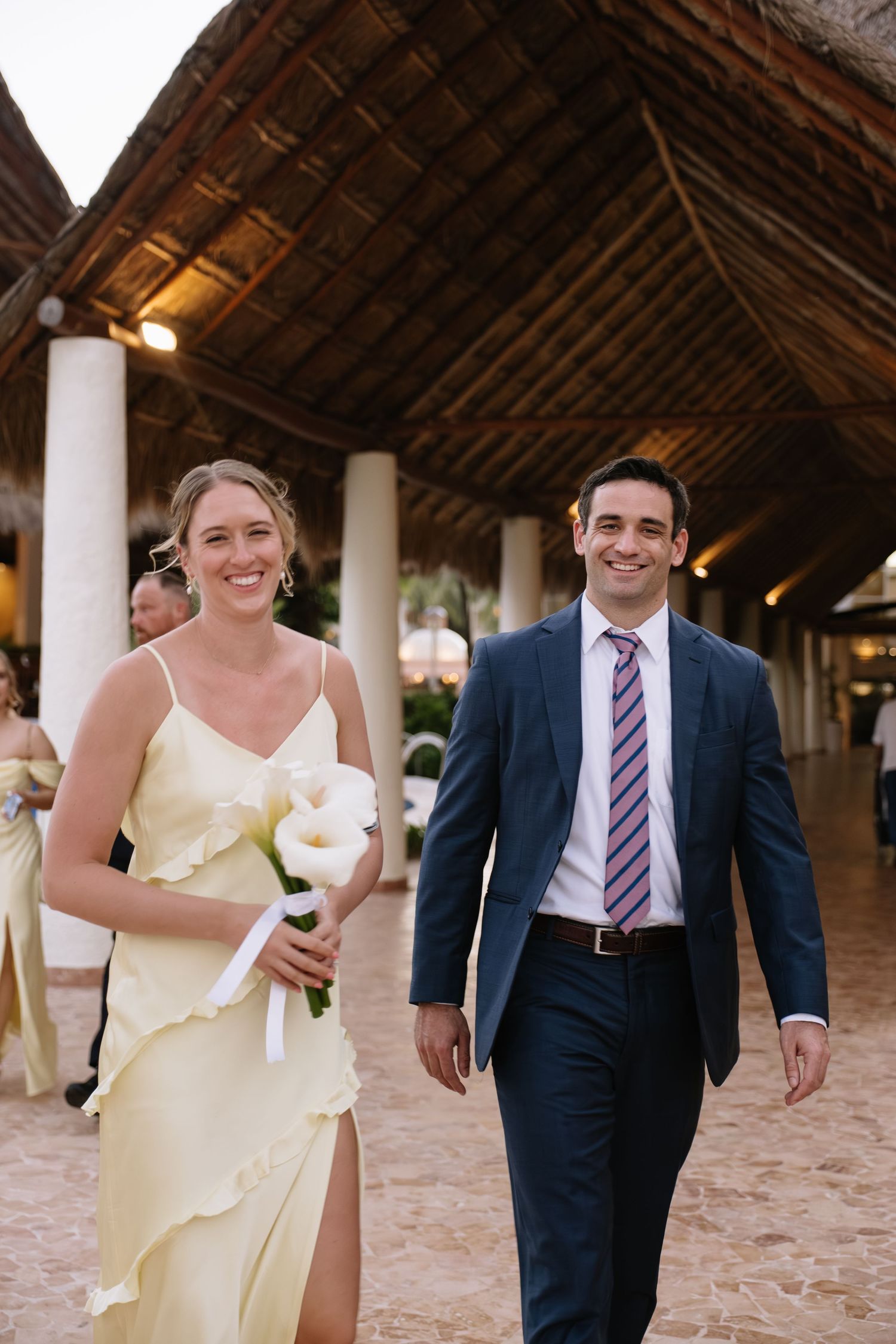 A joyful couple walking along a sandy beach under a covered wooden walkway with warm lighting.