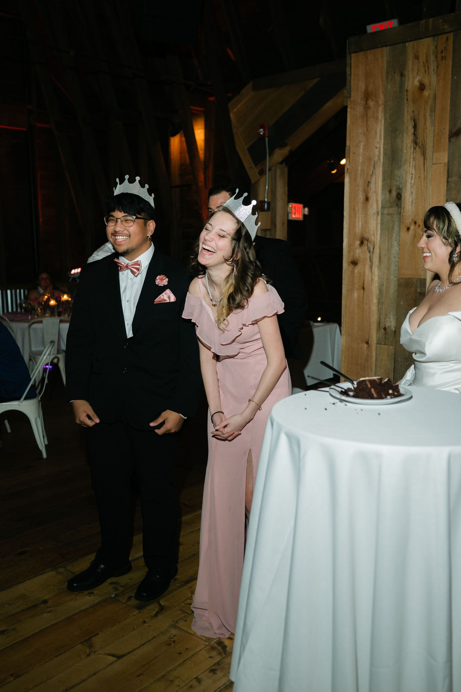 Wedding reception scene in rustic barn venue with guests wearing celebratory crowns.