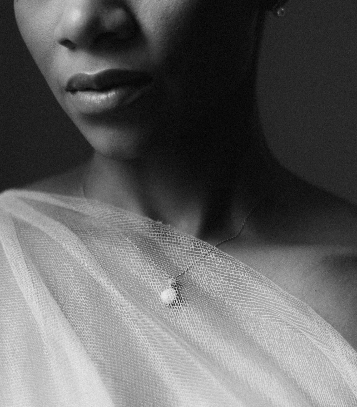 Black and white portrait of a woman wearing a pearl necklace and sheer white tulle fabric draped over her shoulder.