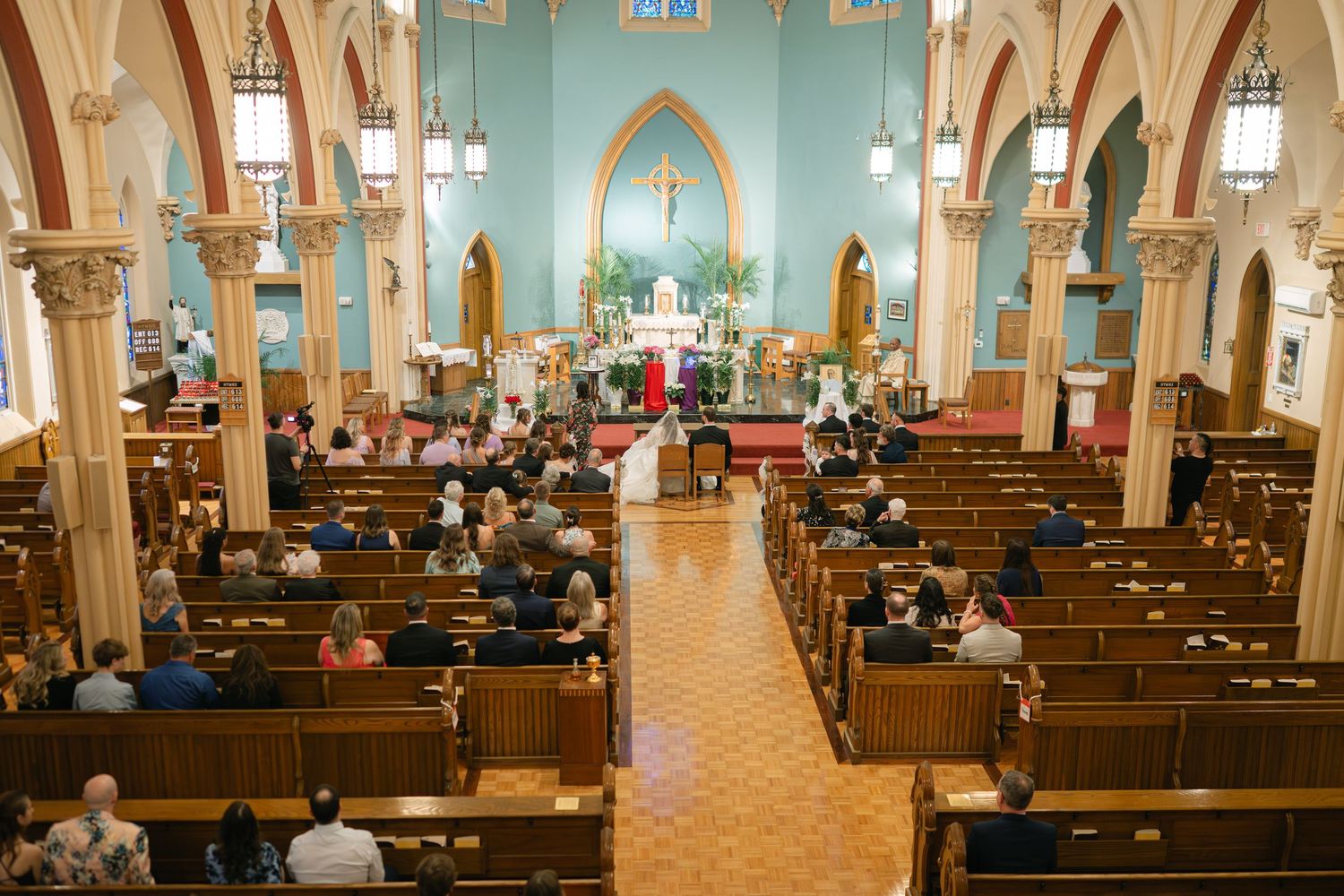 Interior of a grand church with turquoise walls, wooden pews, and arched columns.