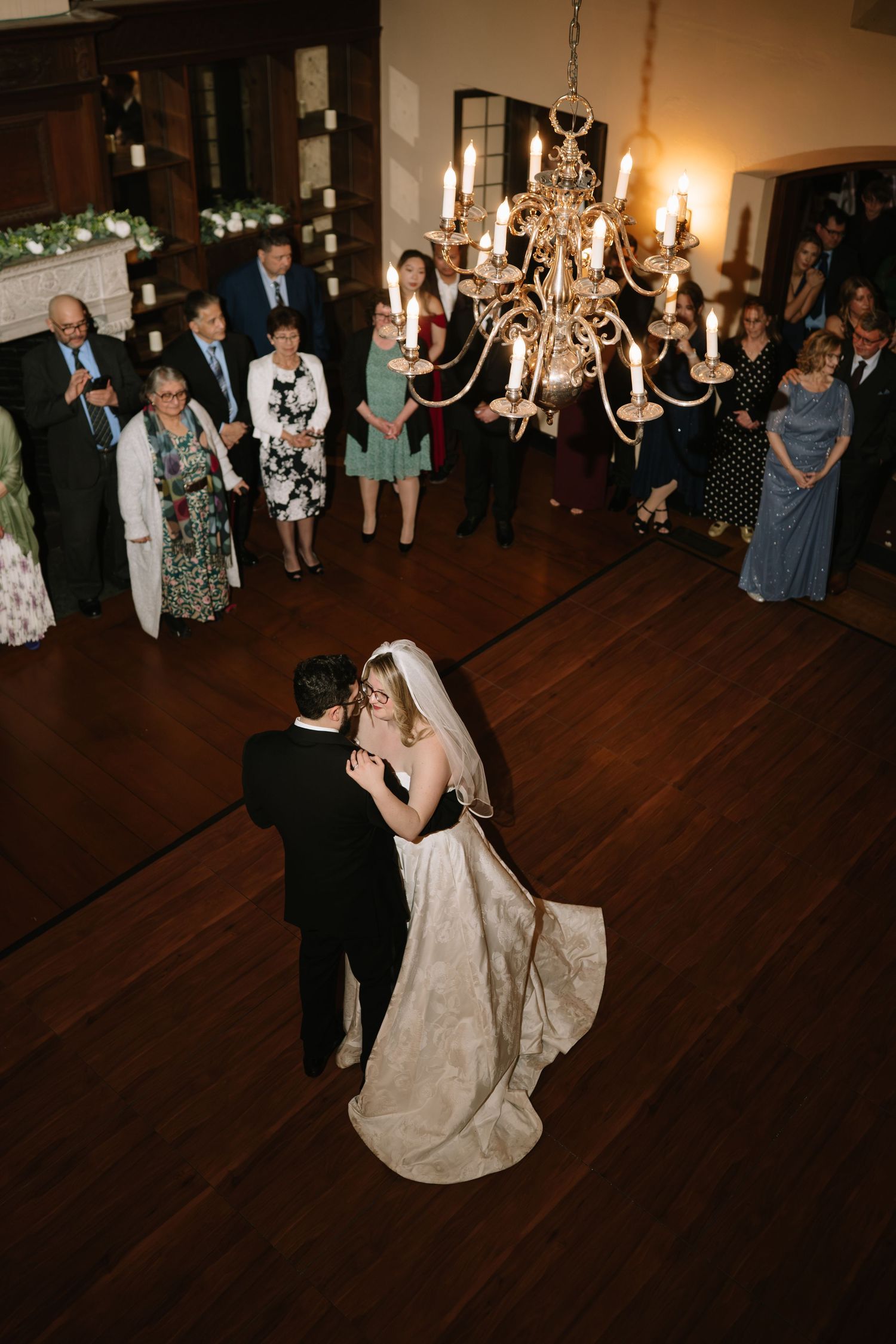 Aerial view of bride and groom sharing their first dance under a chandelier surrounded by wedding guests.