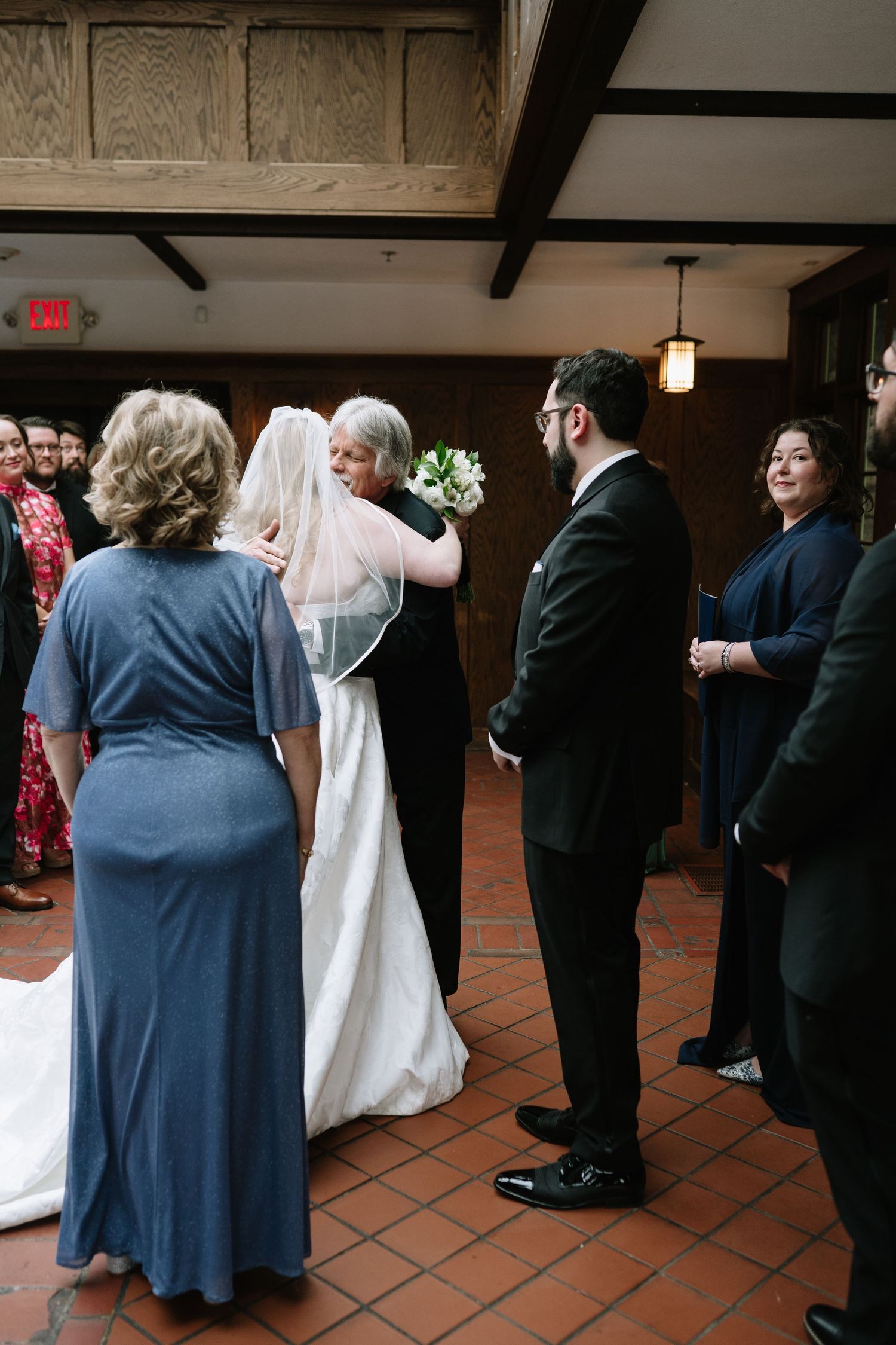 Bride and groom stand at wedding ceremony altar surrounded by guests in elegant indoor venue with terracotta floors.