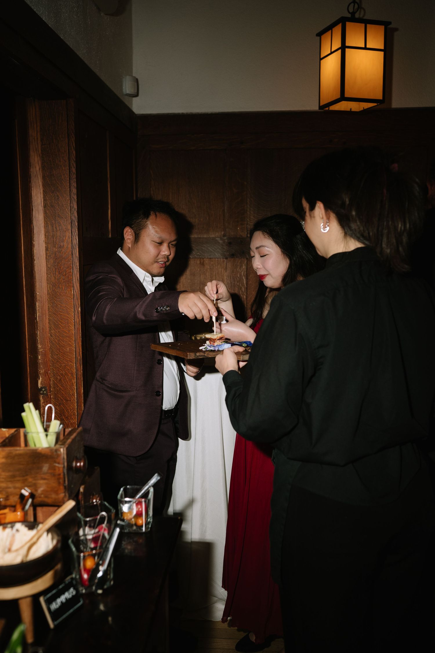 A man in a dark suit serves appetizers to two women at an elegant indoor reception event.