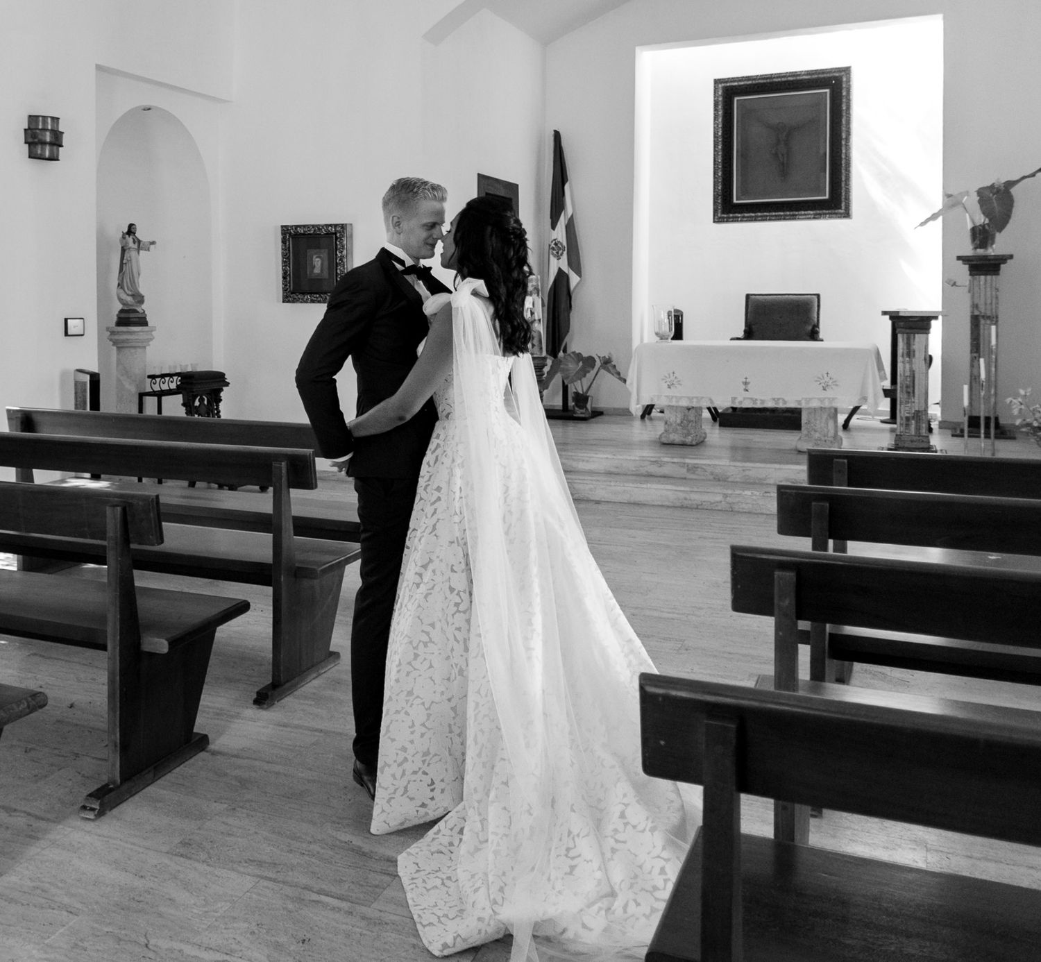 A wedding couple shares an intimate moment in a church with wooden pews.