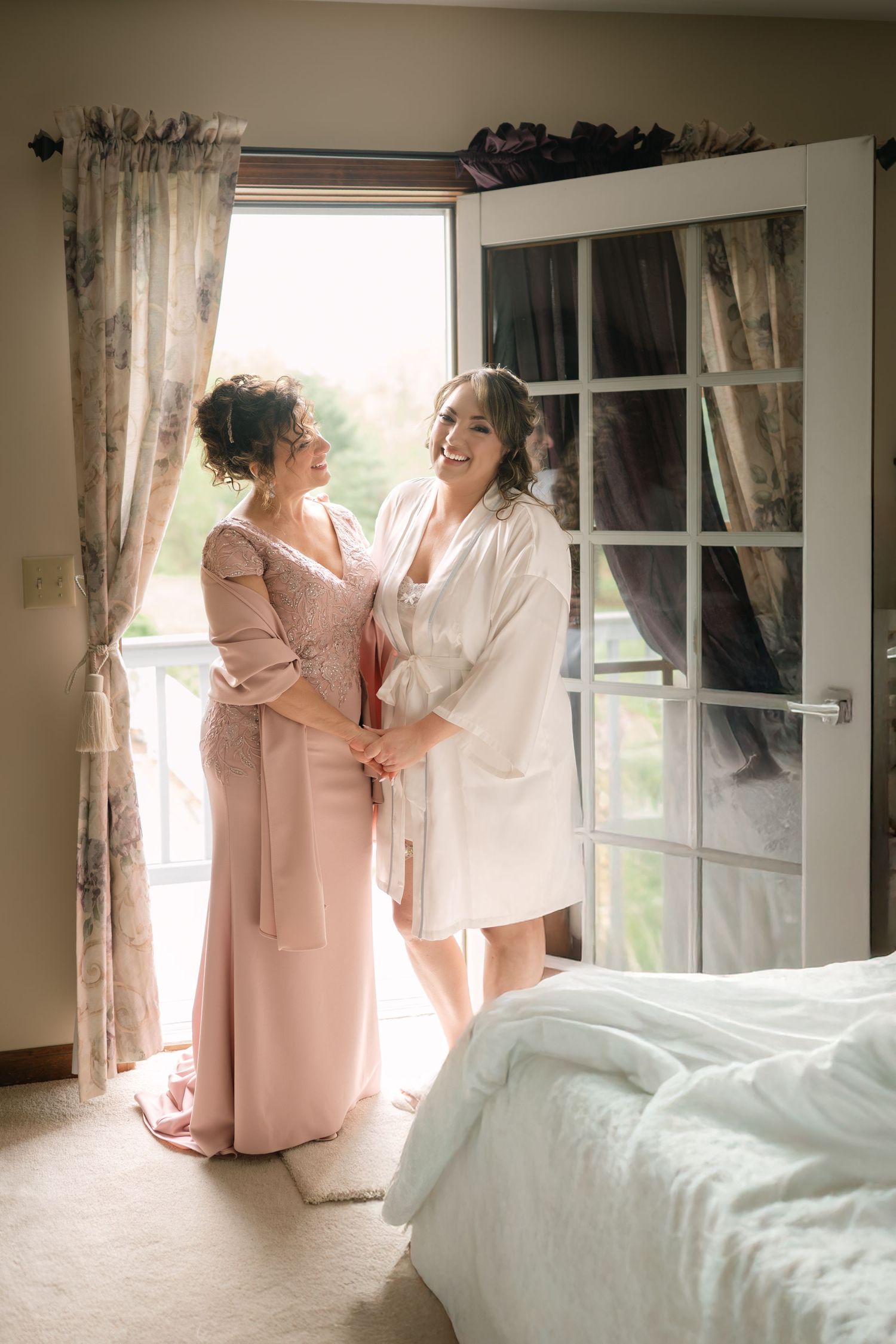 Two people in pink and white robes share a moment by a sunlit window.