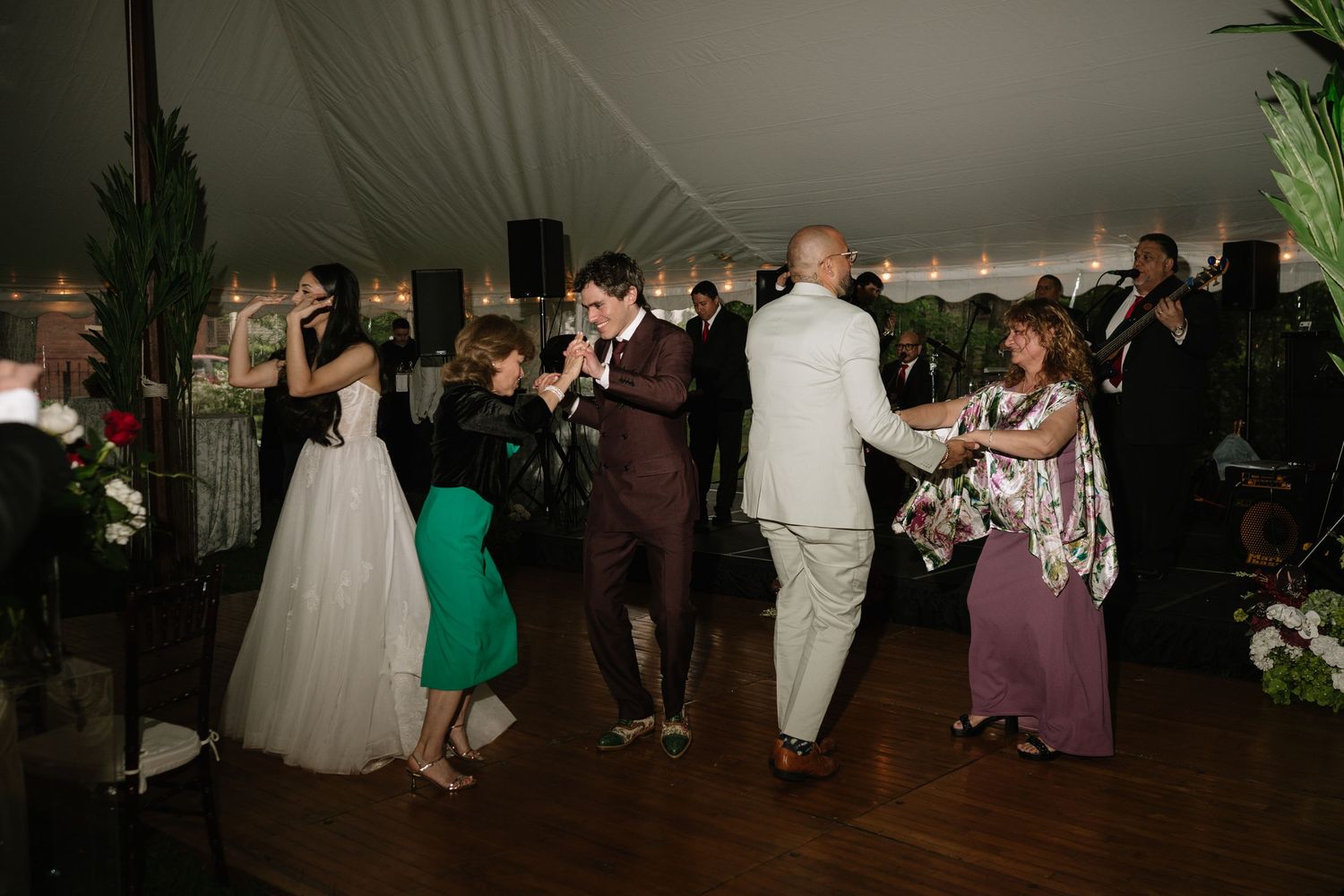 Guests dancing joyfully at a wedding reception under a white tent.