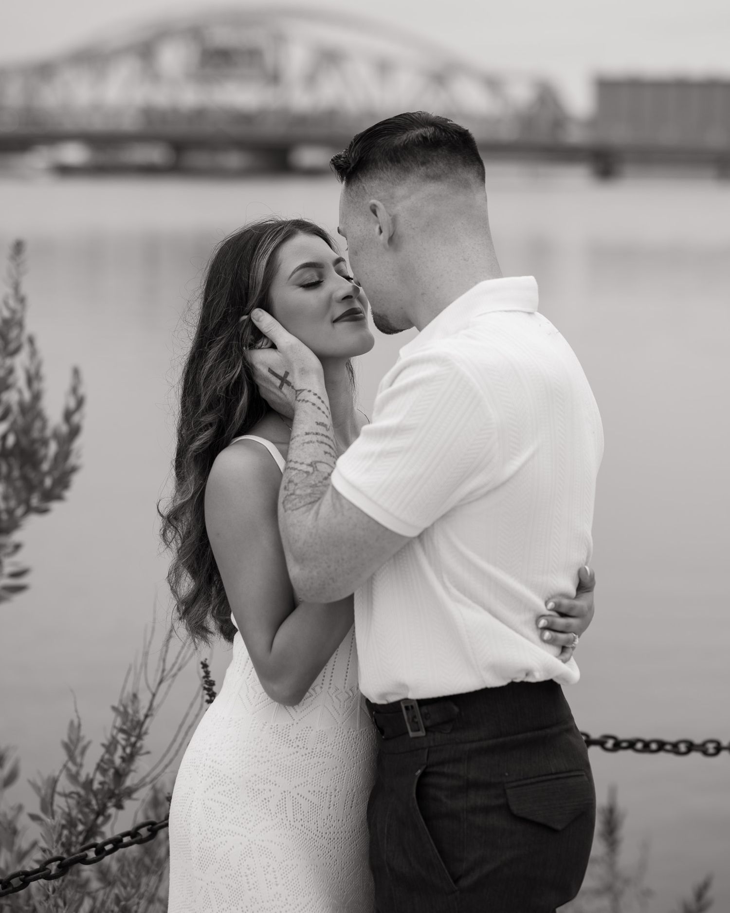 Black and white portraits of couple embracing by waterfront railing.