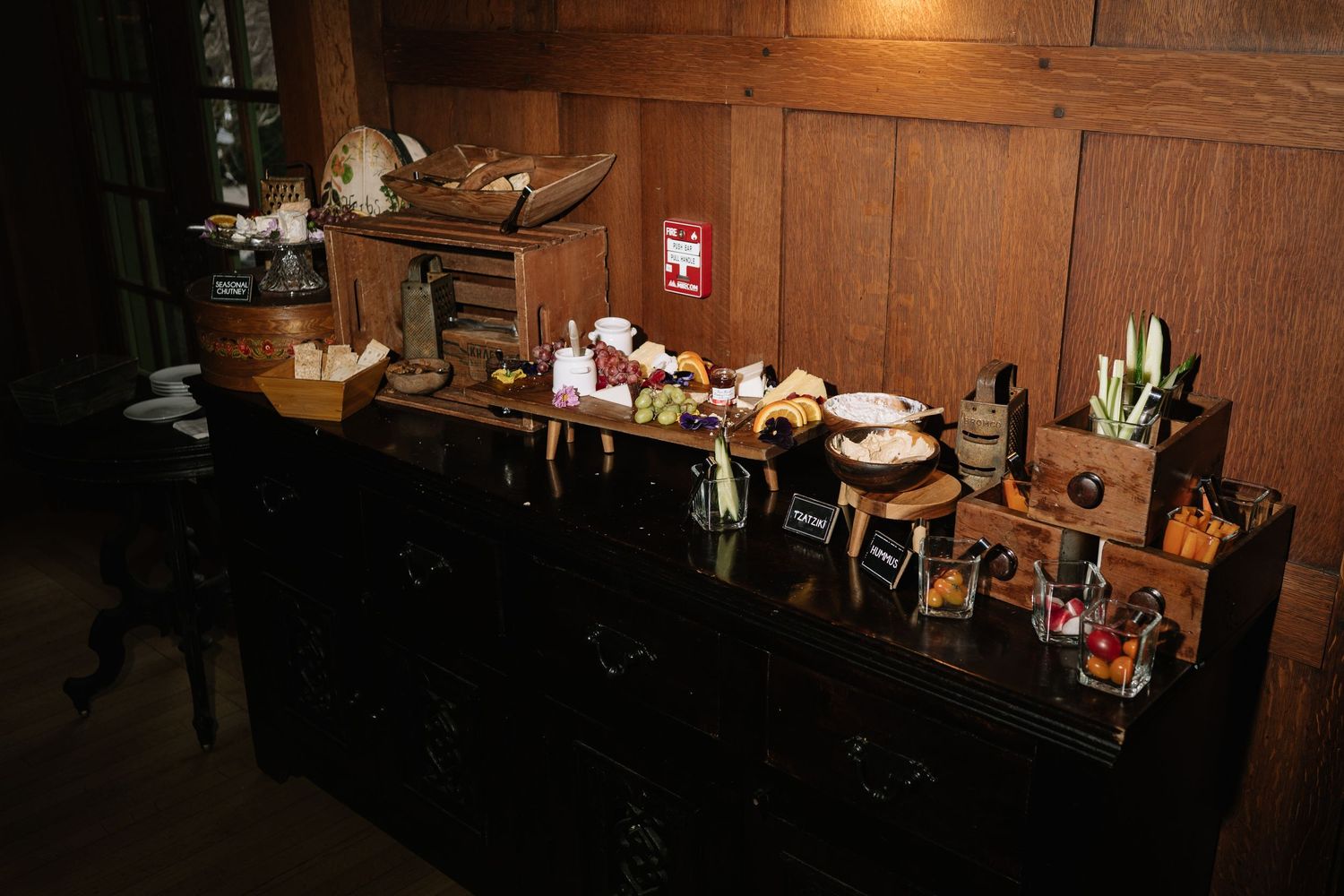 Dark wooden buffet table displaying assorted food items, condiments, and decorative chef figurines in a dimly lit room.