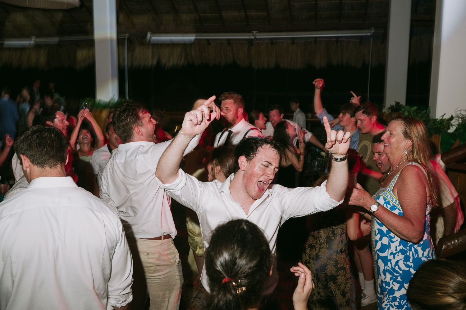 Guests dancing and celebrating on a crowded reception dance floor with arms raised.
