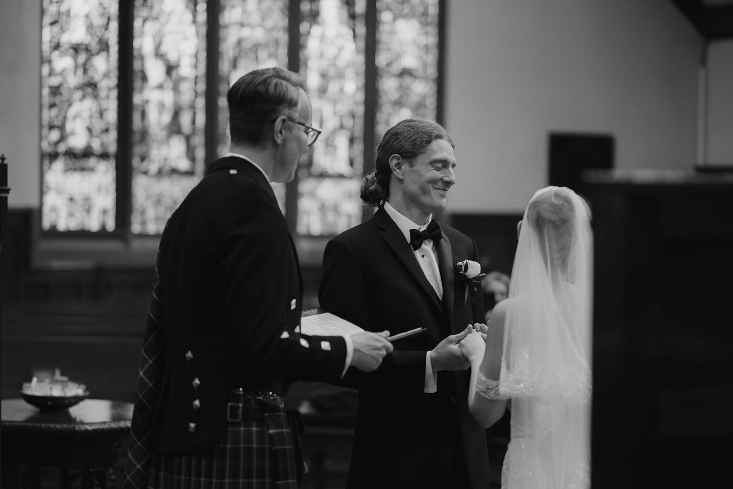 Wedding party members gather in formal attire near large windows in a church setting.
