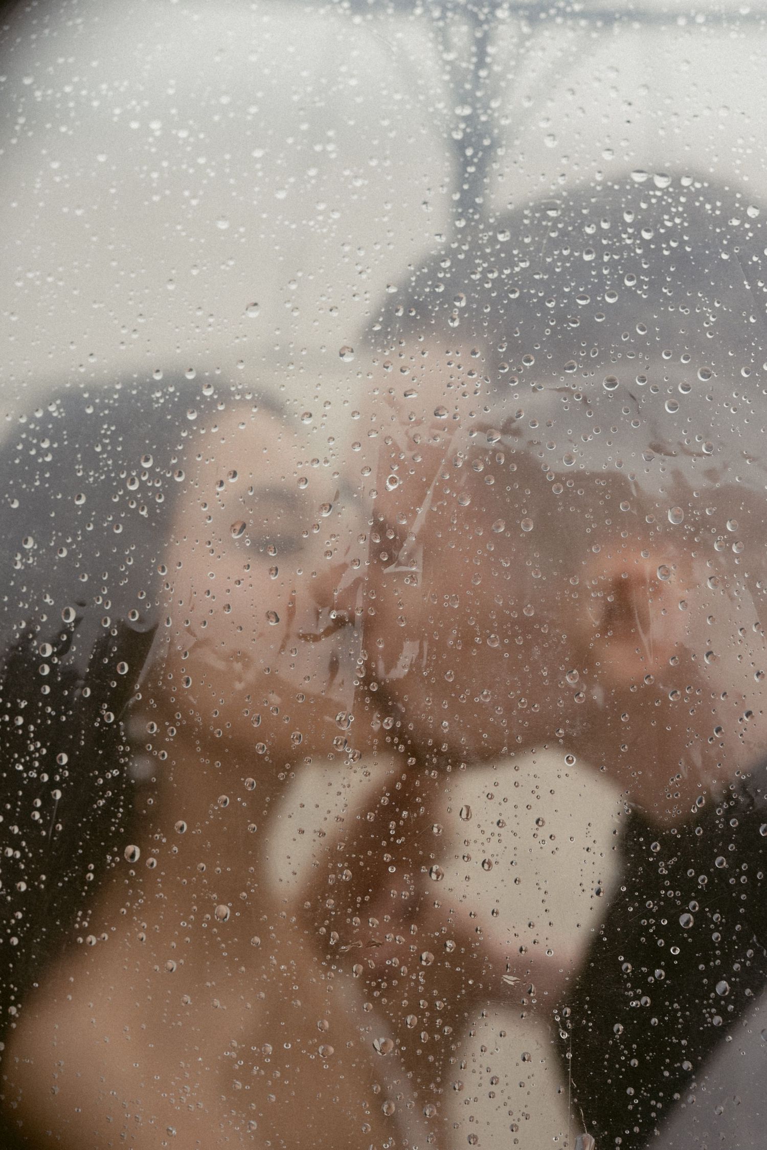 Romantic couple sharing an intimate moment behind a rain-covered window creating a dreamy, soft-focus effect.