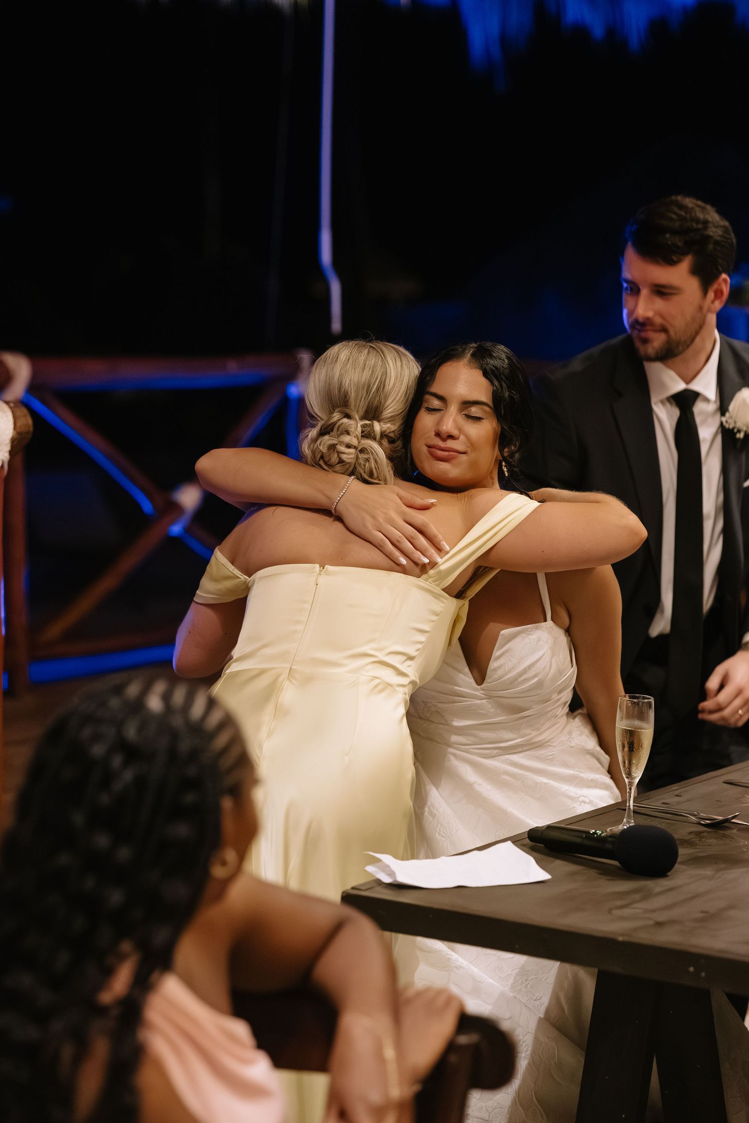 Wedding party members in formal attire seated at a dark wooden table during reception celebration.