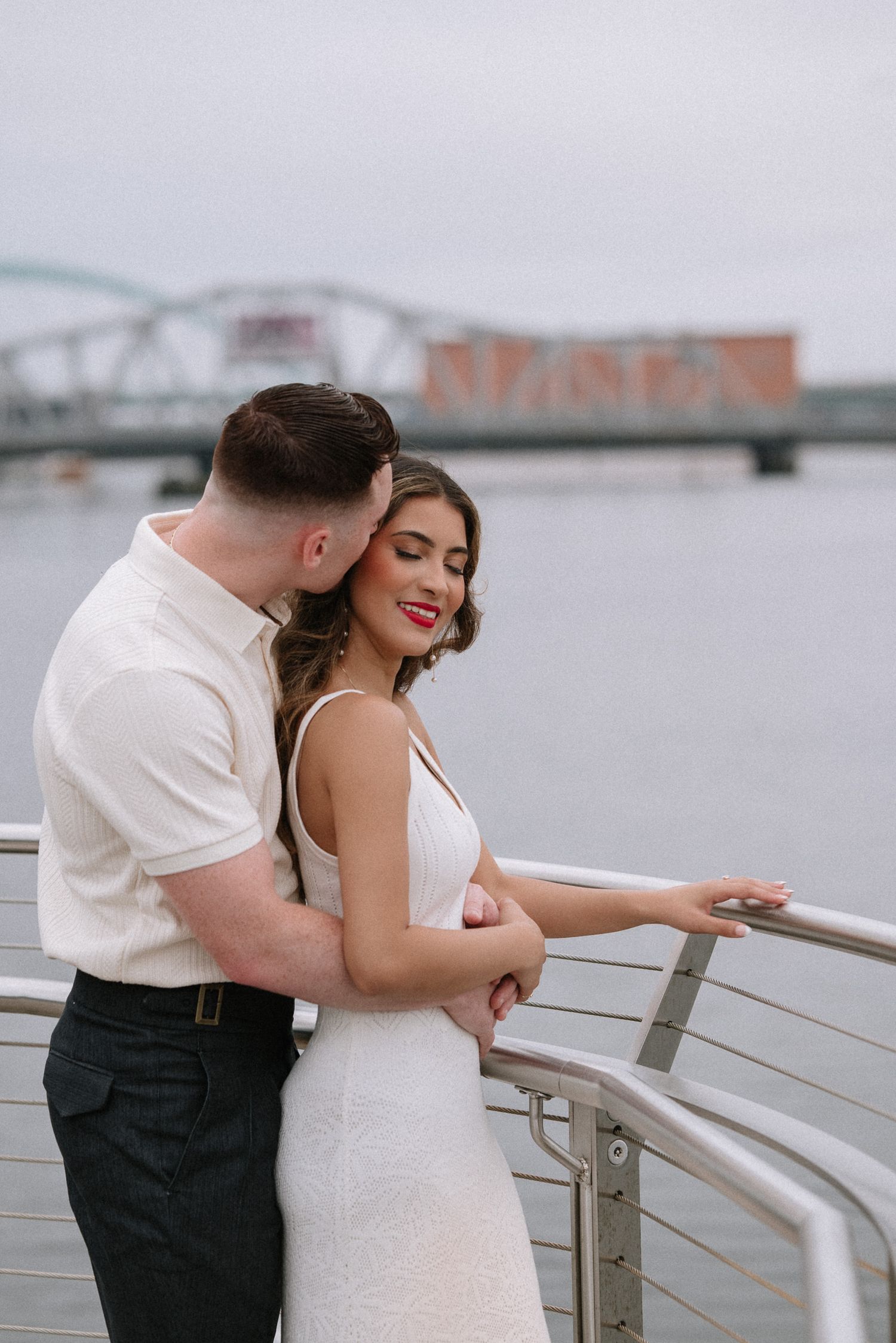 Romantic couple embracing on waterfront boardwalk during engagement photo session.
