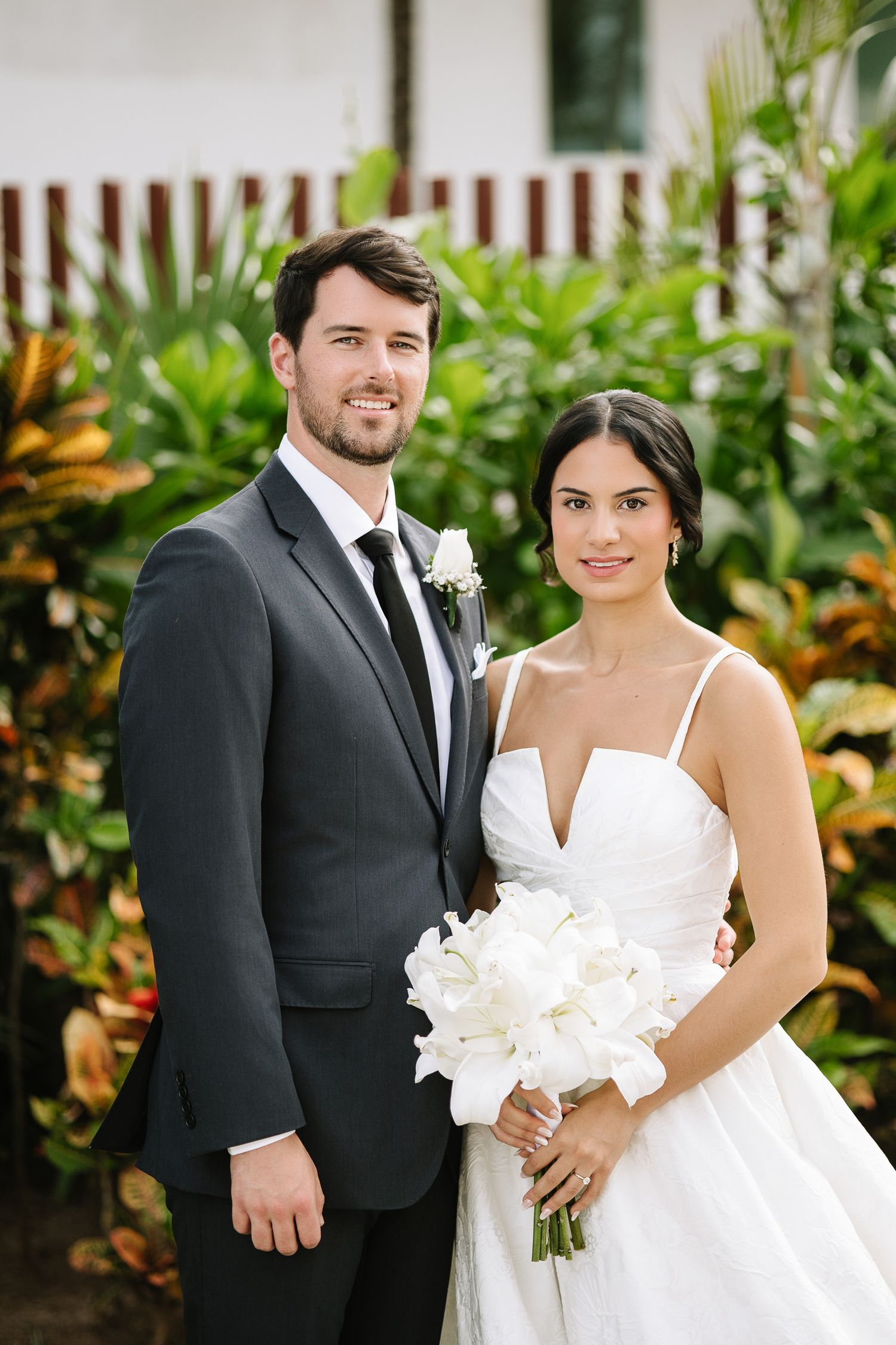 Wedding couple posing in lush tropical garden setting with white floral bouquet.