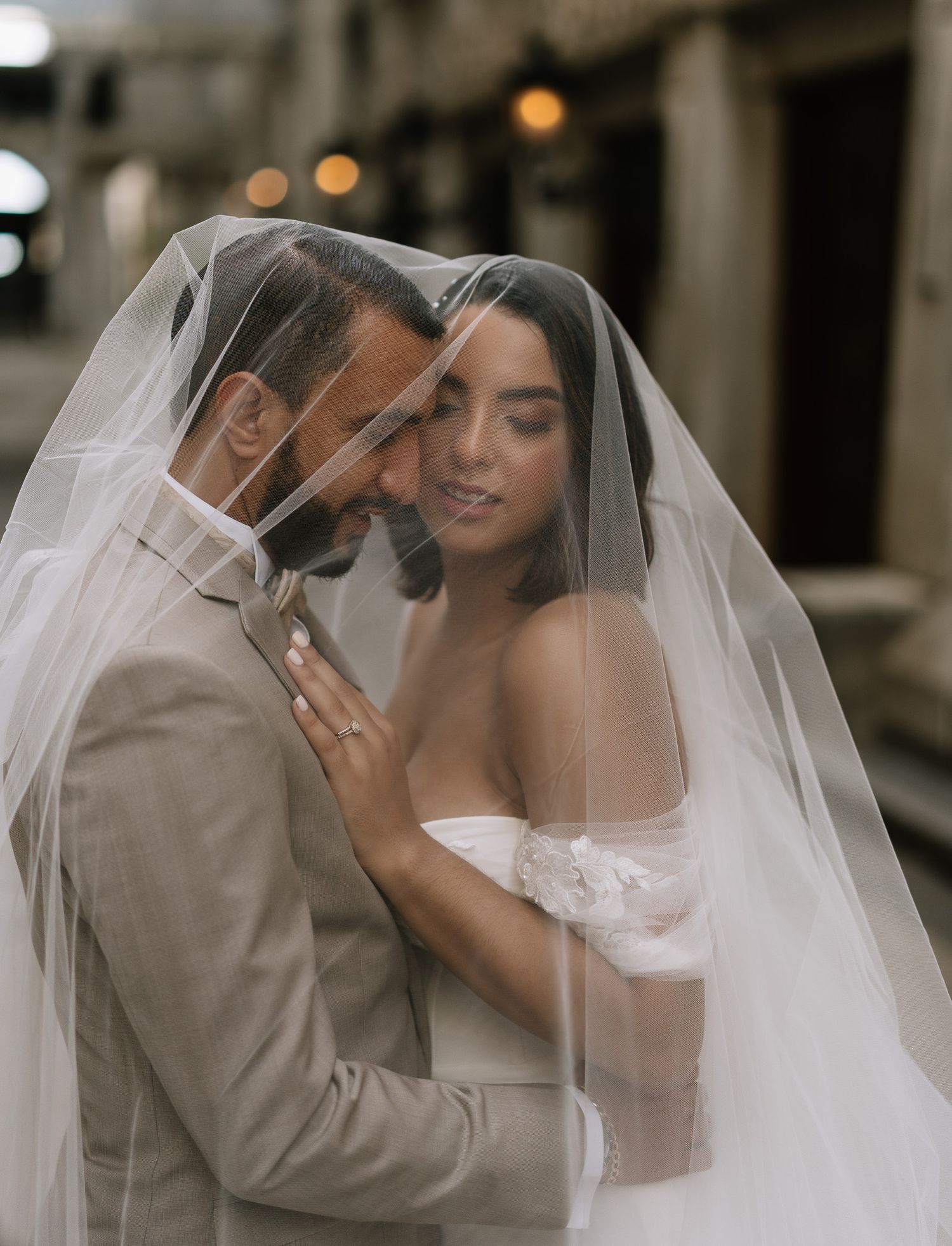 Bride and groom share an intimate moment under a flowing white veil on their wedding day.