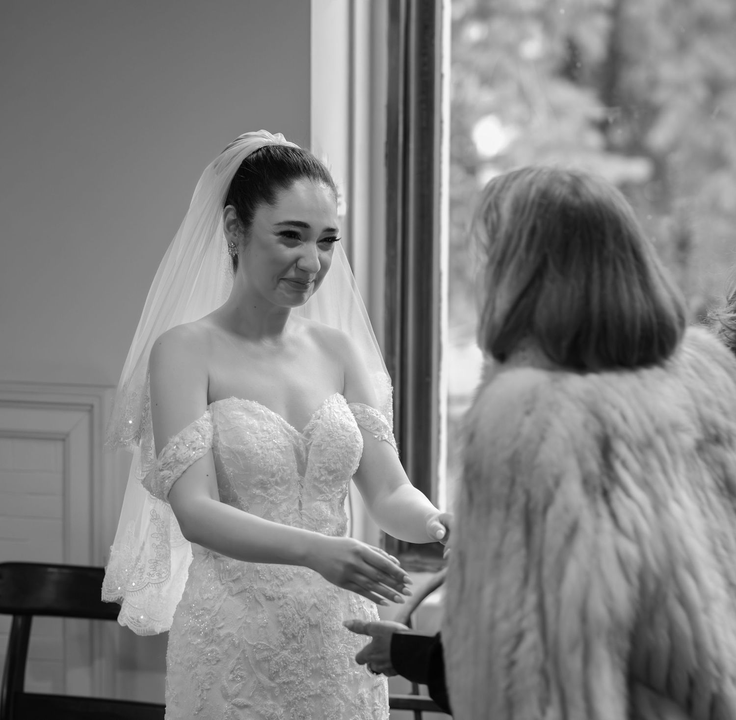 A bride in a white lace wedding dress gets ready in a sunlit room before her ceremony.